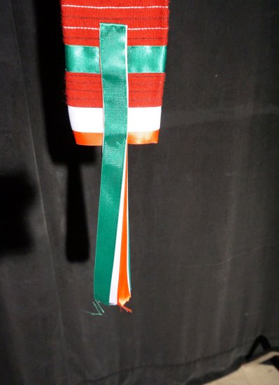A man's red fabric belt with green, white and red silk ribbons.