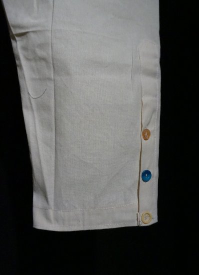 Close up of a man's white linen pants, with multicolored buttons along the ankle.