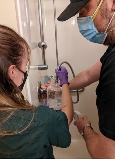 Noelle Horth is holding a jug up to a shower to sample it for Legionella.