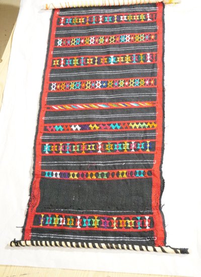 A red and black weaving with multicolored embellishments on a small loom.