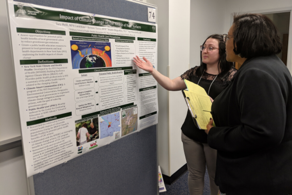 A student stands in front of her research/internship poster, explaining her work to a faculty member who listens attentively.