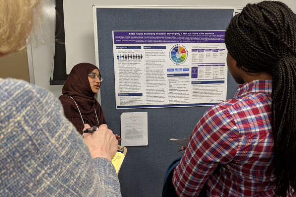A student stands beside her poster, speaking with two women who are looking at her poster.