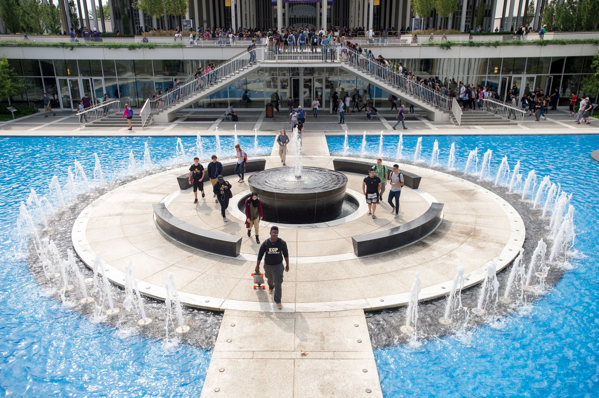 Students walk on a pathway surrounded by a large fountain in the center of campus