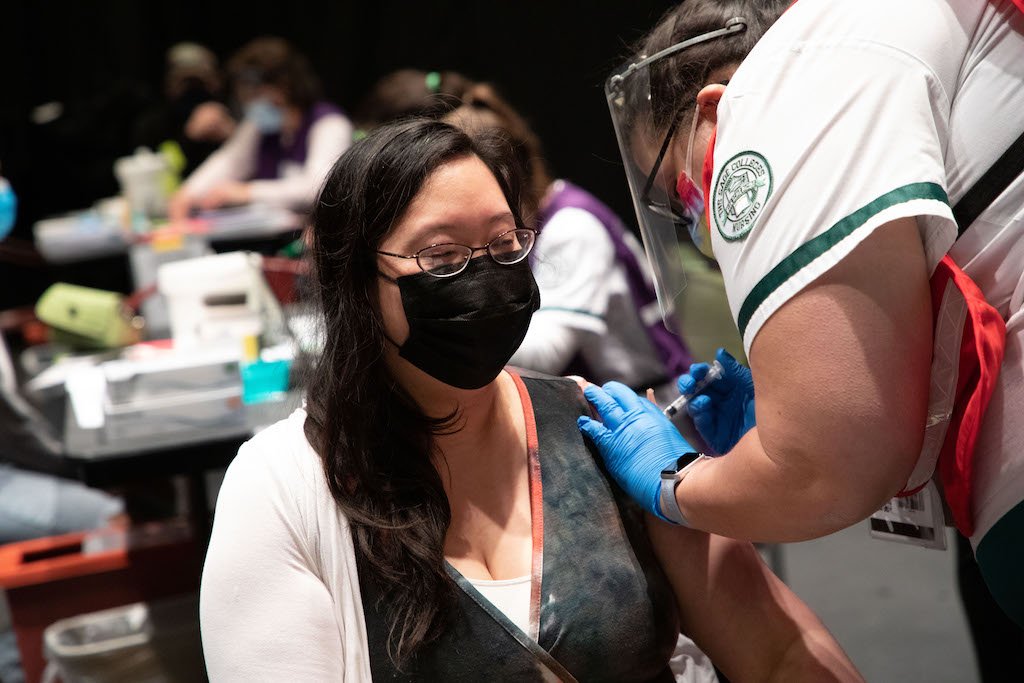 A woman, masked, receiving a vaccination