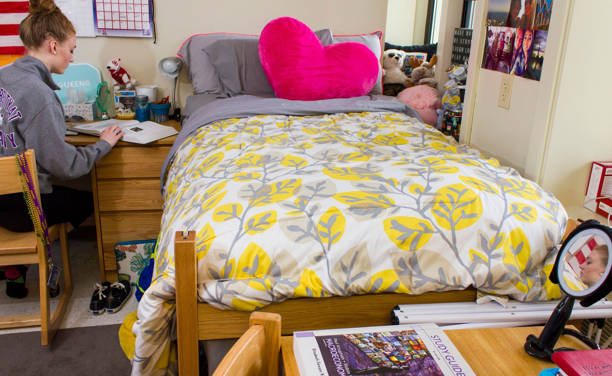 A student works at her desk inside her residence hall room, sitting beside a made bed
