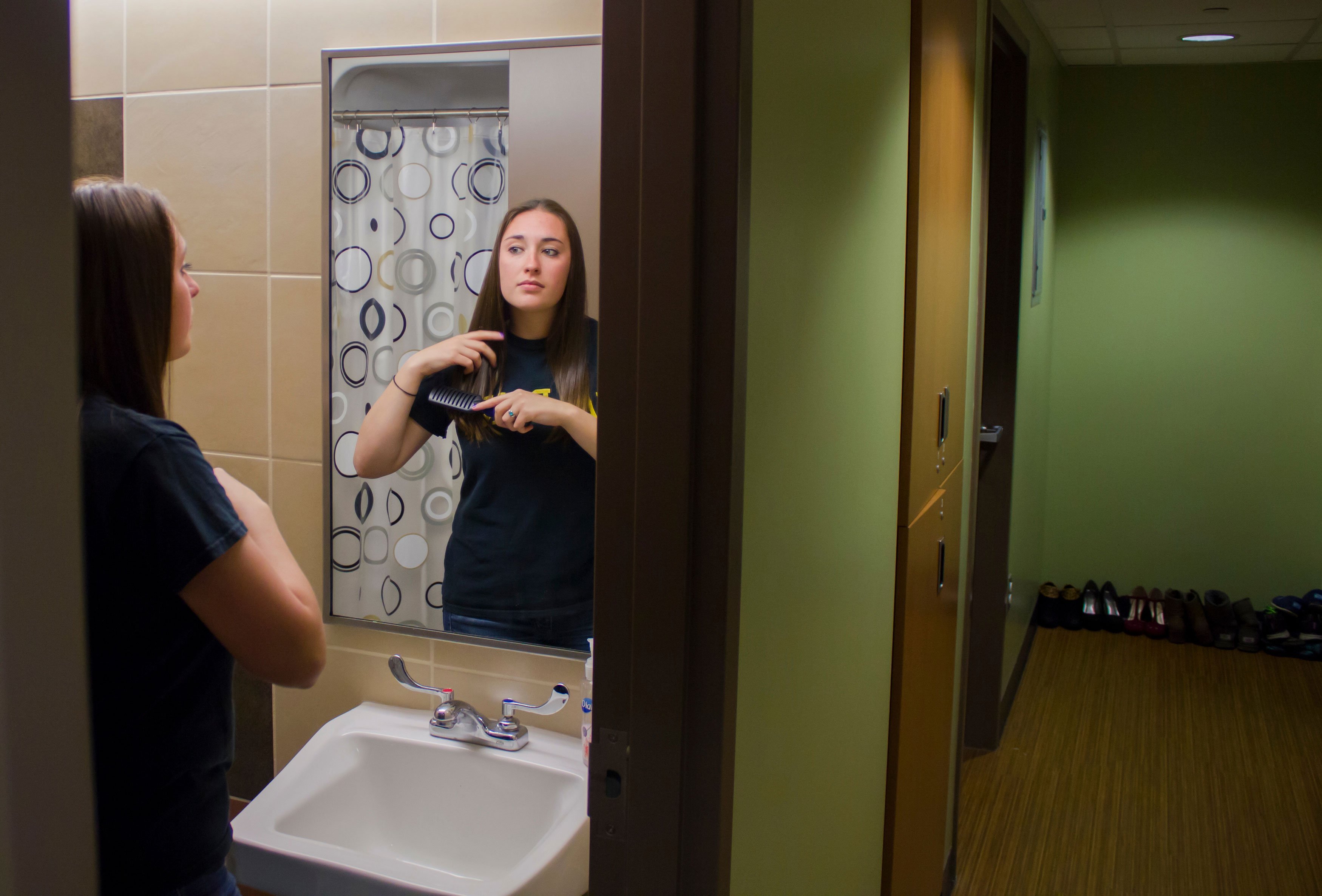 A student brushes her hair in front of a bathroom sink and mirror inside a Liberty Terrace apartment