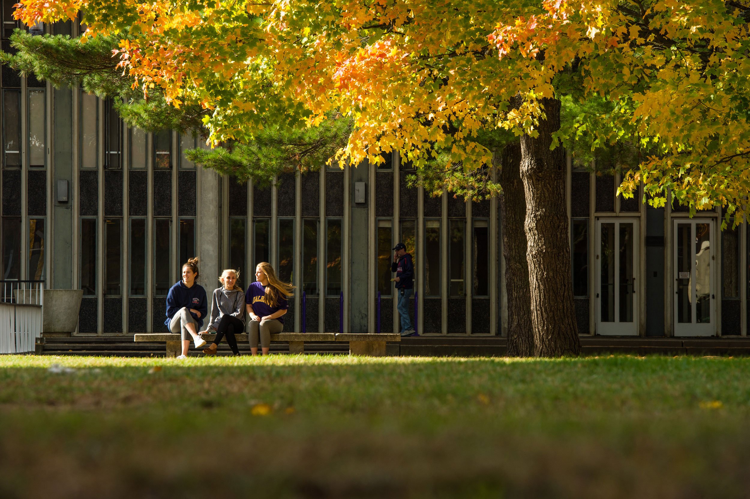 Three students sit on a bench outside Dutch Quad amid fall foliage