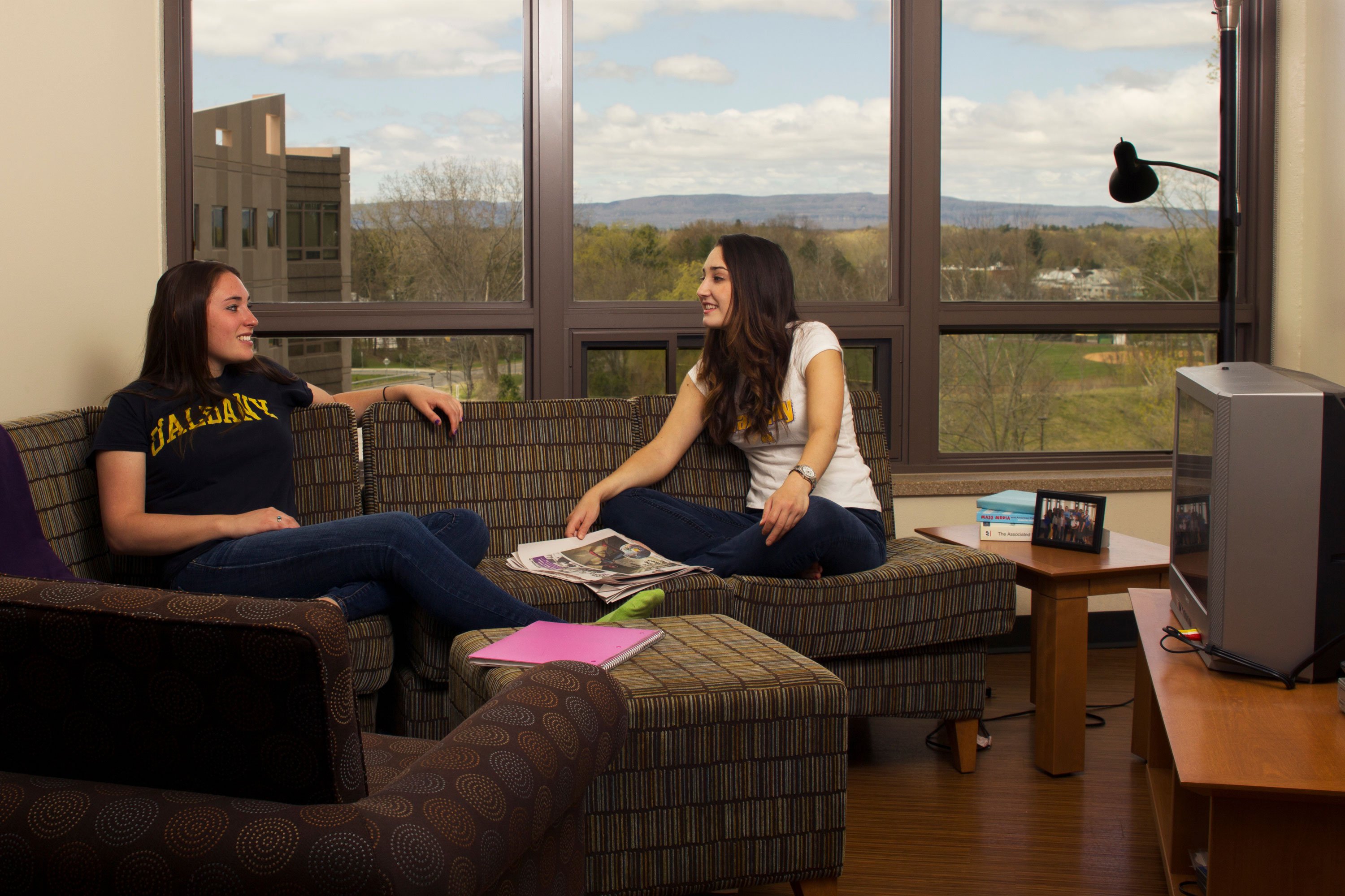 Two students sit on living room couch near a TV inside a Liberty Terrace apartment