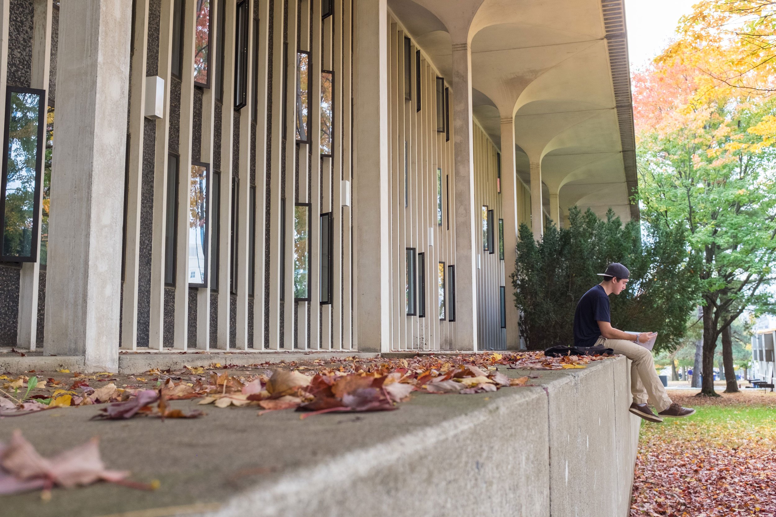 A student sits on a wall outside Indigenous Quad studying, with his feet hanging over the edge