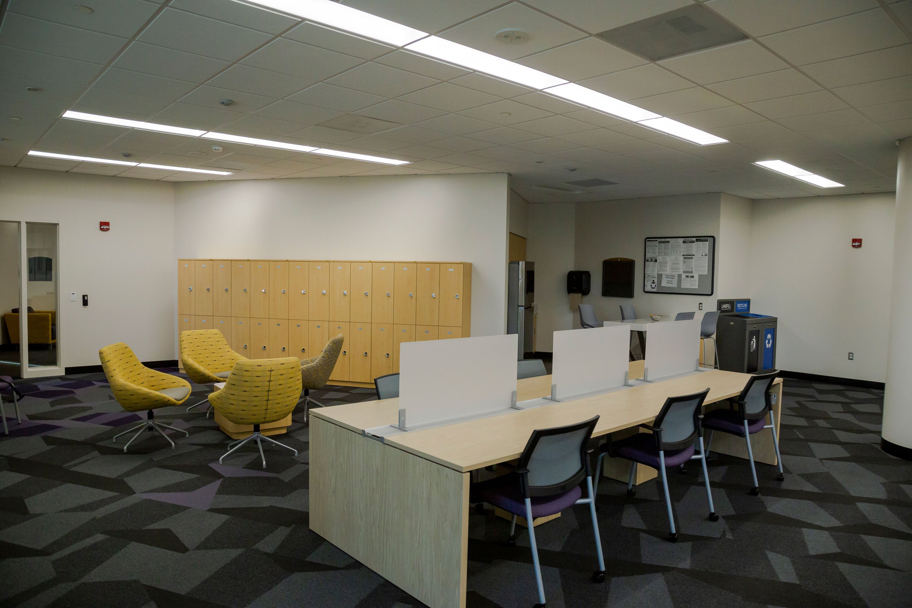 The inside of the UAlbany Innovation Center, with four yellow chairs around a coffee table, a workstation with six chairs, and a row of wooden lockers.