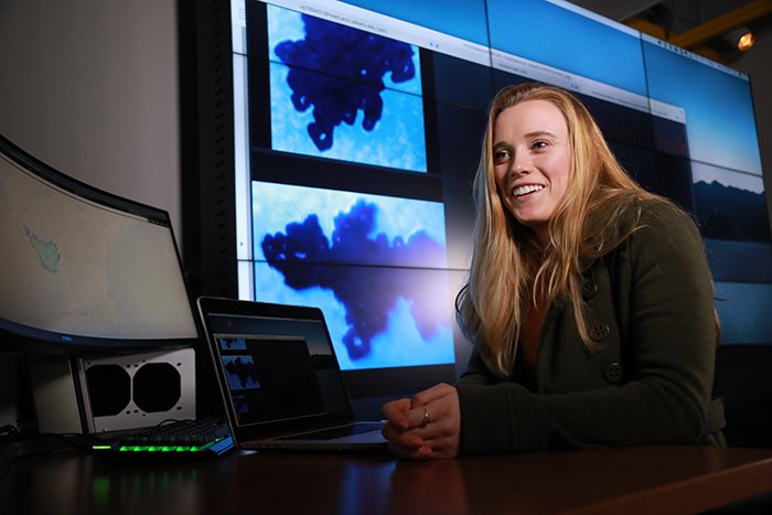 Vanessa Przybylo, a PhD research assistant at ASRC sitting in front of large weather screens in the xCITE Lab.