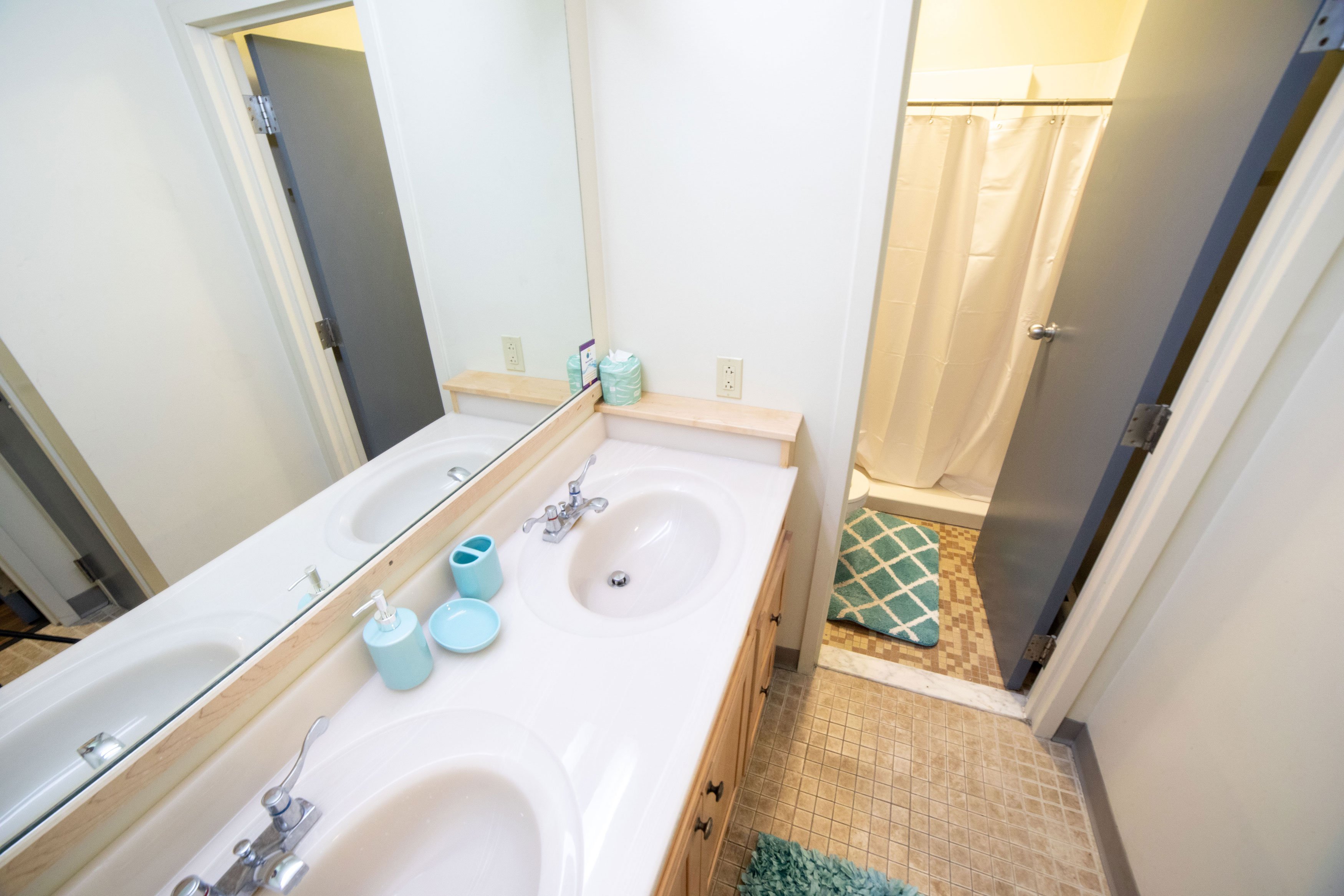 A two room bathroom, with a double sink and mirror in the first room and a toilet and shower in the second room.