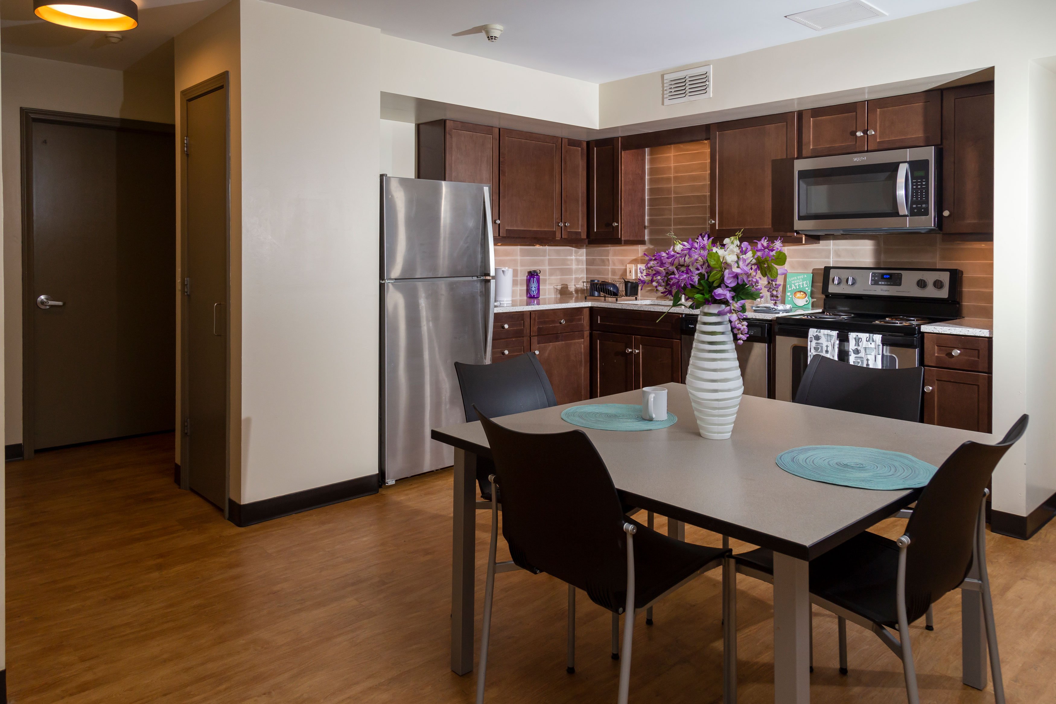 An upgraded kitchen inside an Empire Commons apartment, with stainless steel appliances, dark wood cabinets and a four-seater table.