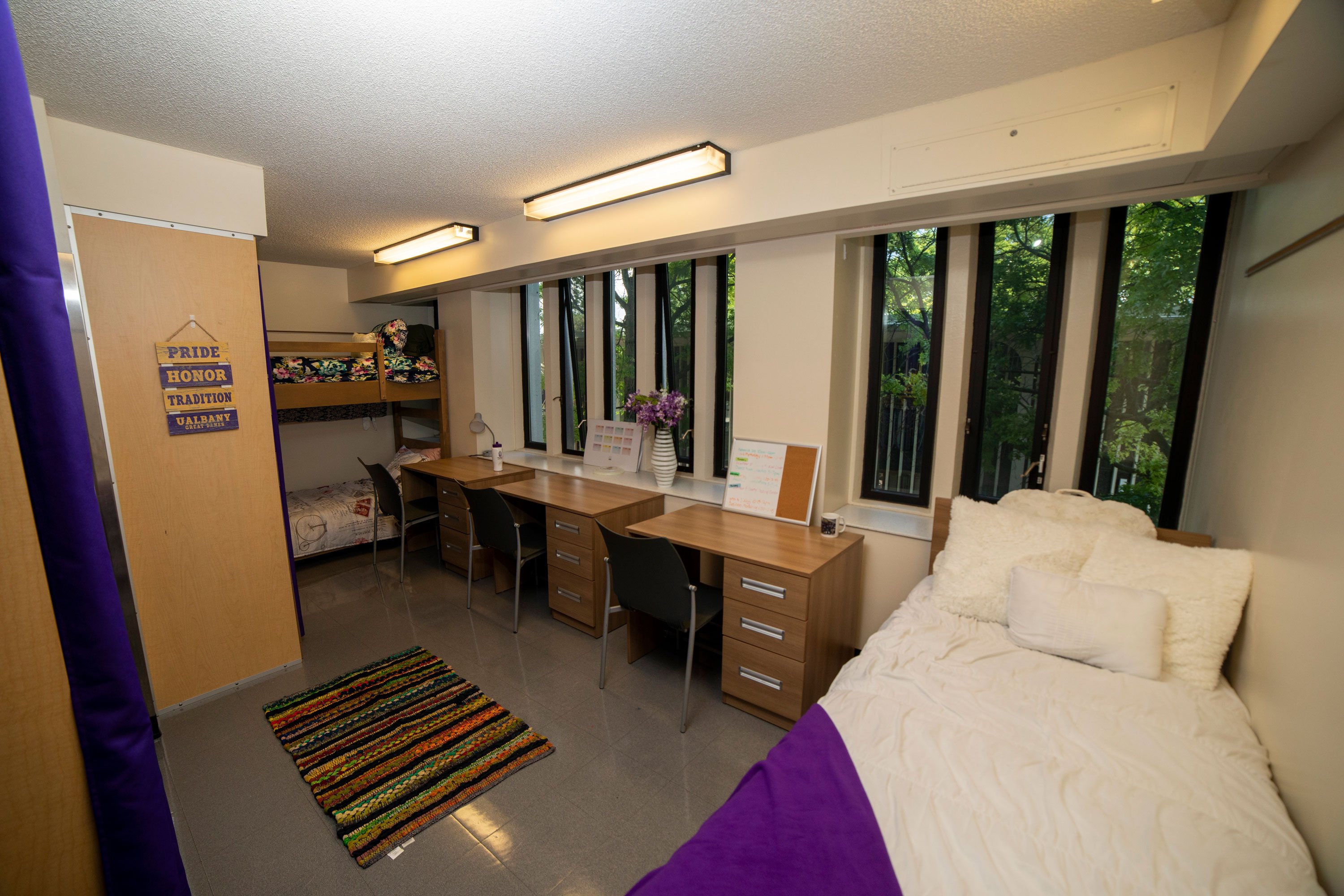 A triple bedroom, with a twin bed, twin bunk beds, three desks and three chairs.
