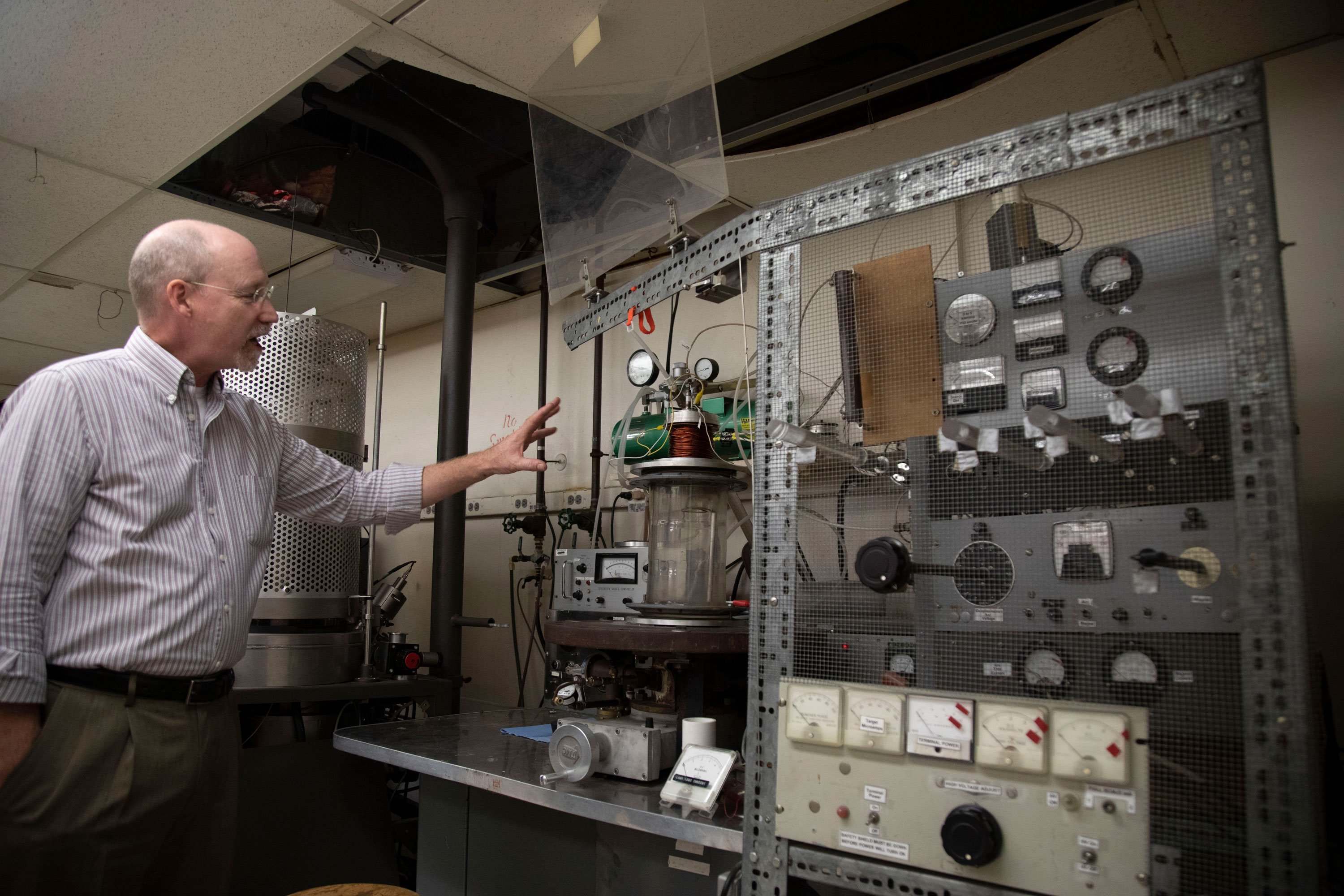 Project Manager Kevin Wynne gestures at equipment on a shelf inside the Ion Beam Lab.