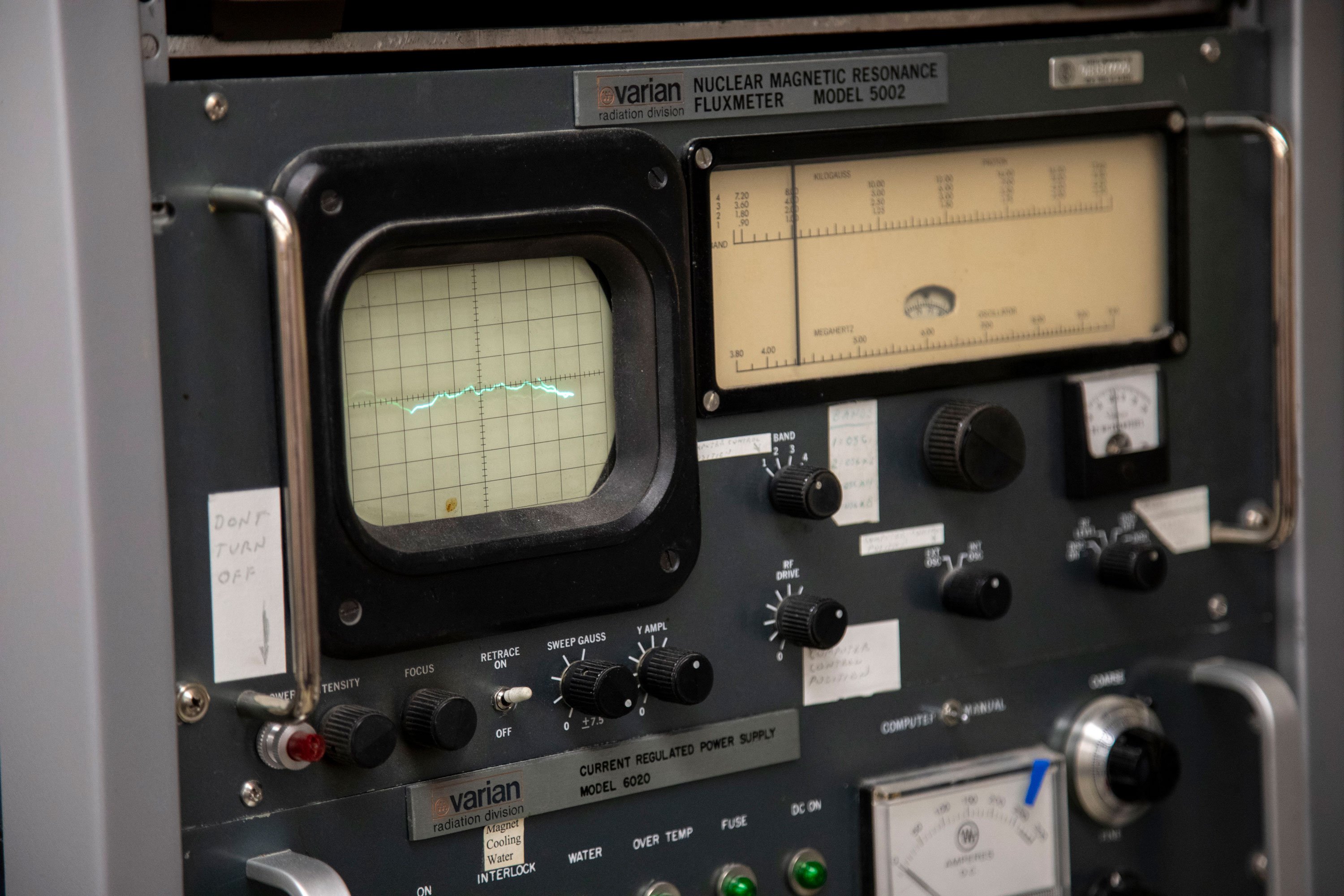 A control board with multiple dials and a display showing data. The label says Varian Nuclear Magnetic Resonance Fluxmeter Model 5002.