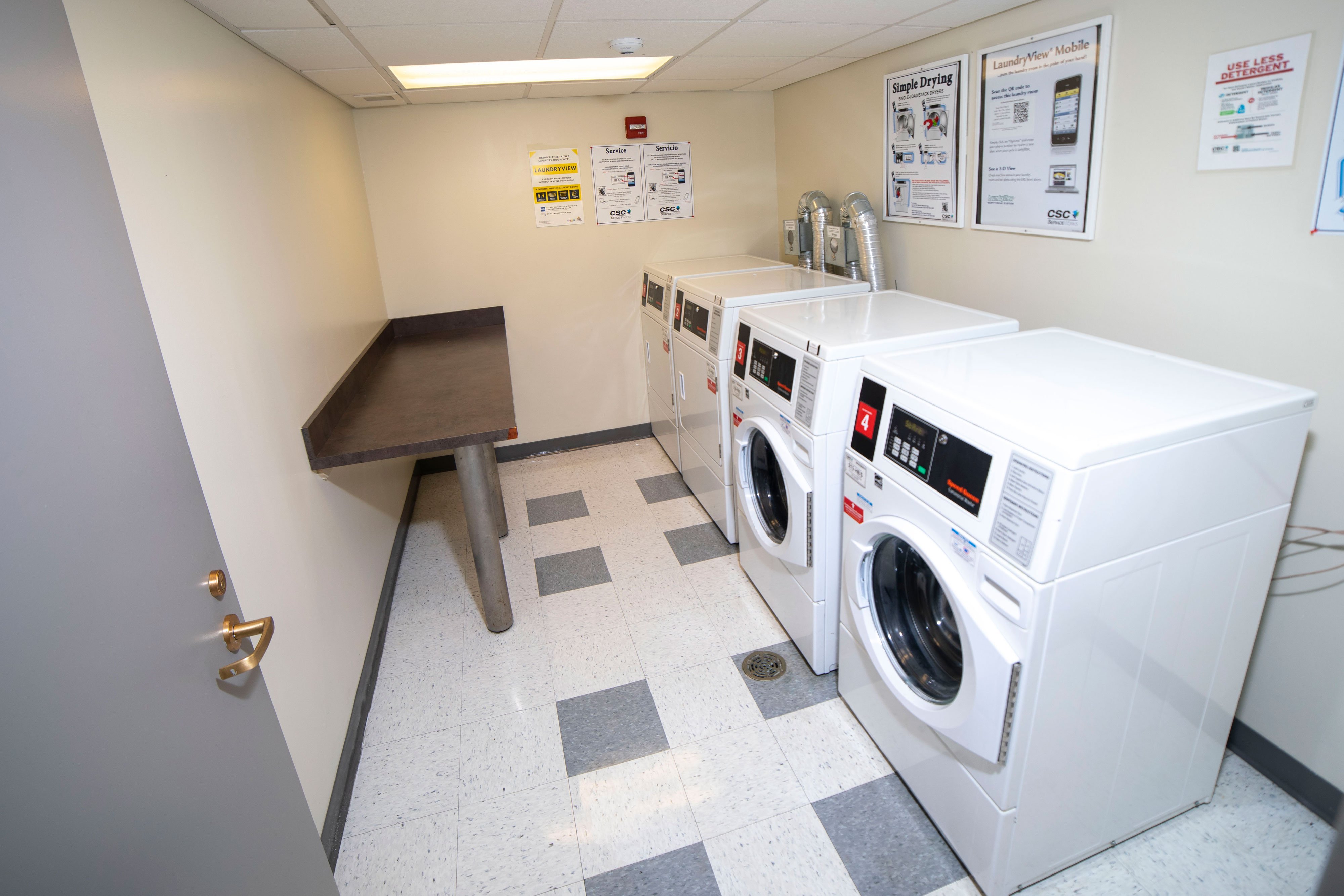 A laundry room with two washing machines, two dryers and a counter top.