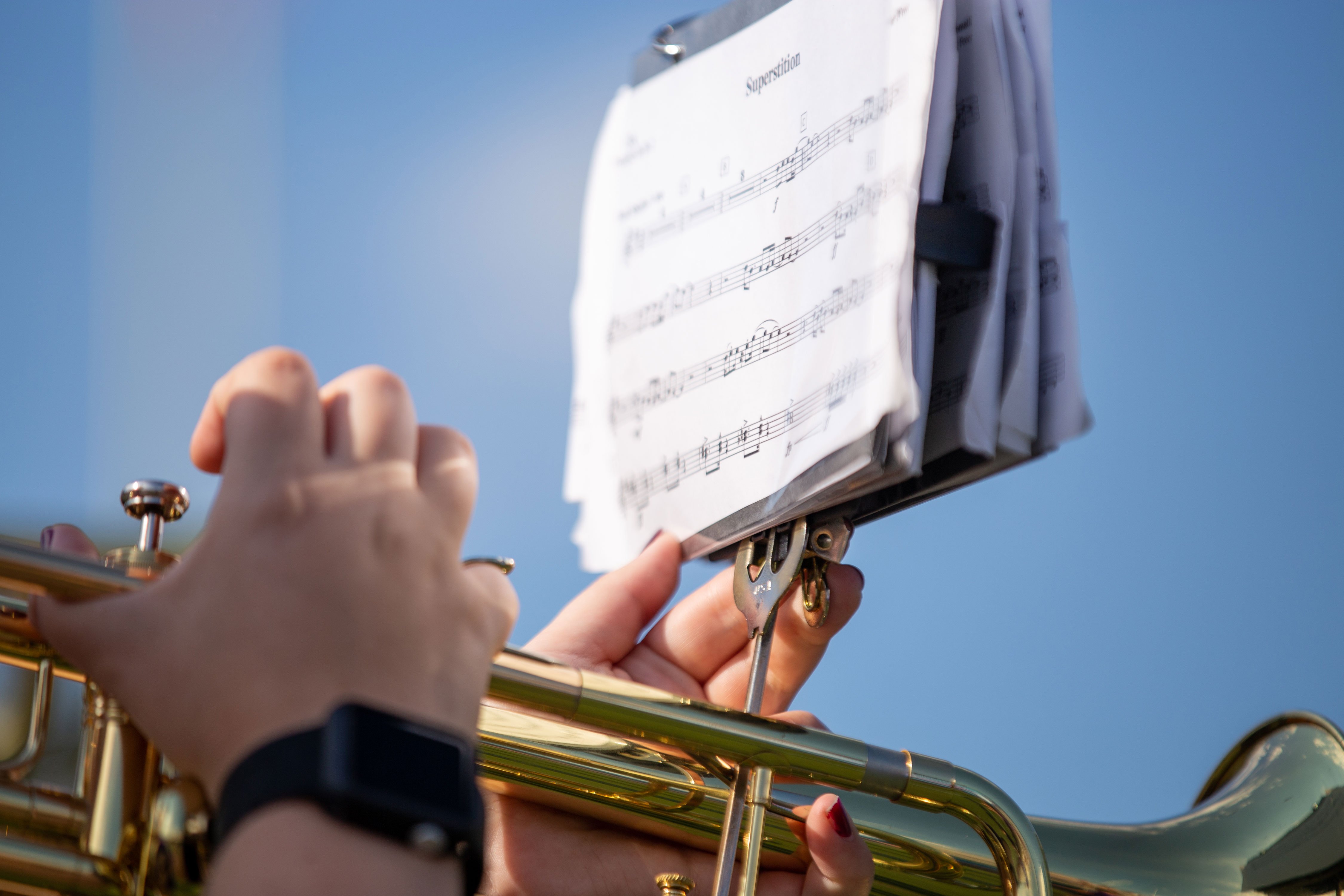 A close-up of "Superstition" sheet music mounted on a trumpet being played by a student.