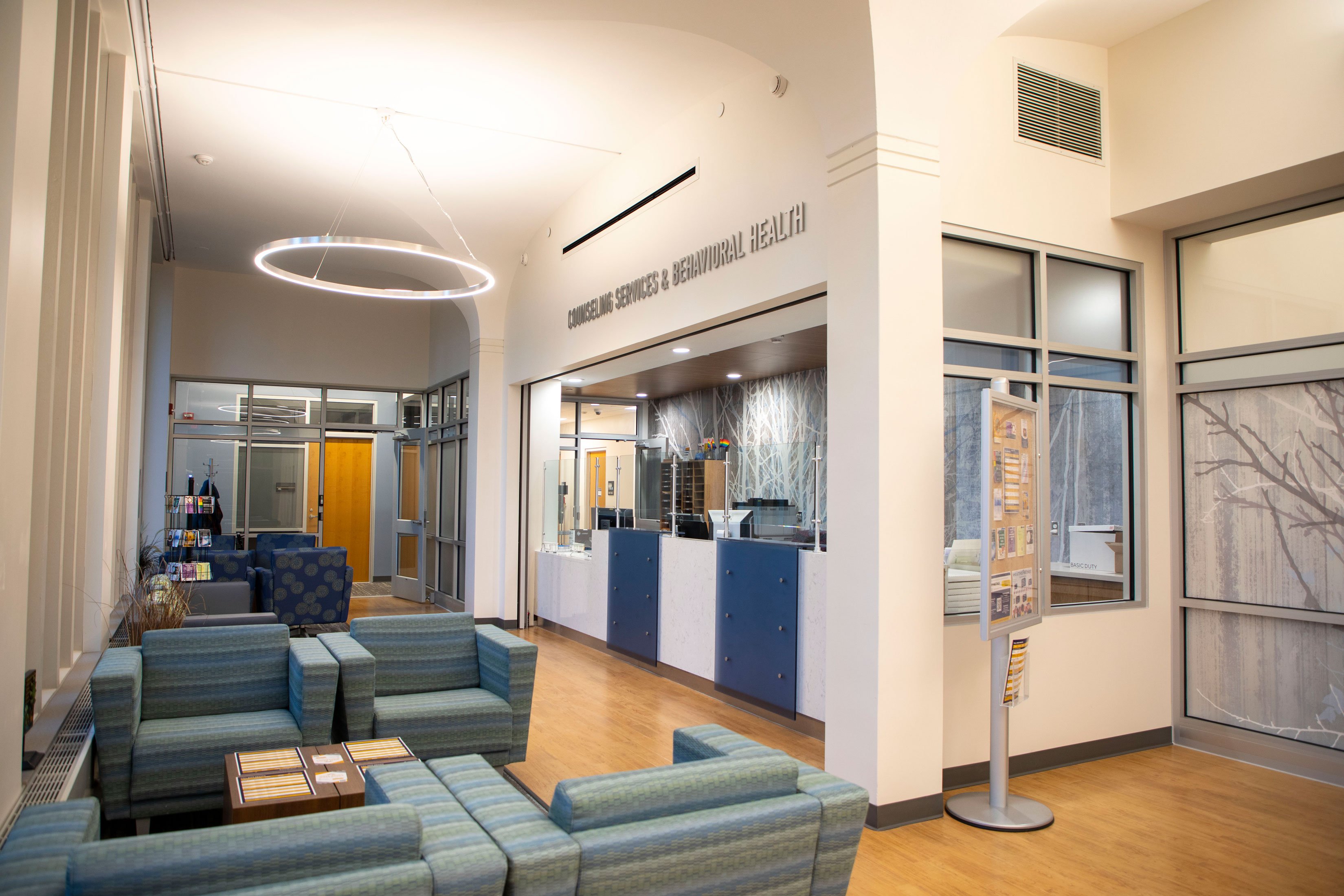 A check-in desk with the words "Counseling Services & Behavioral Health" mounted above and armchairs situated nearby.
