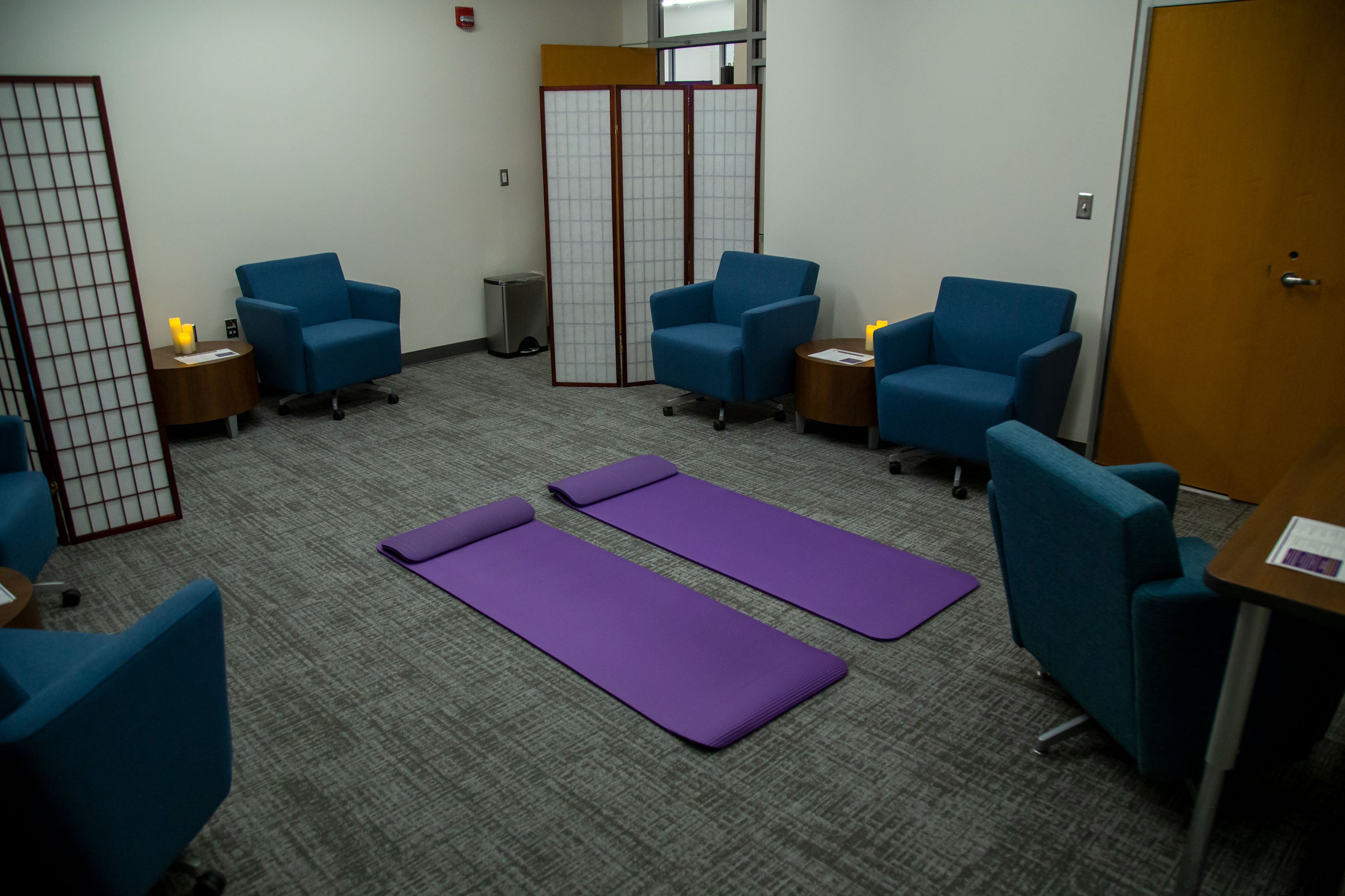 A room with dimmed lights, yoga matts, comfortable chairs and battery-operated candles.