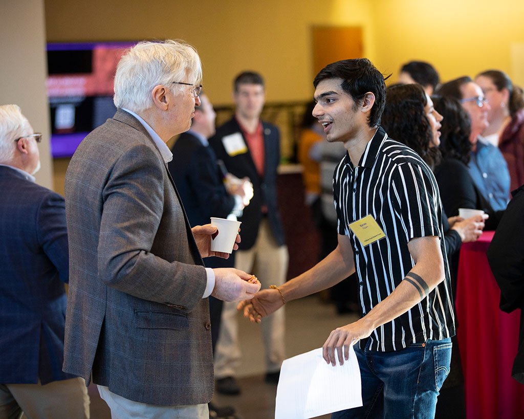 The featured student speaker at the event shakes hands with a faculty member.