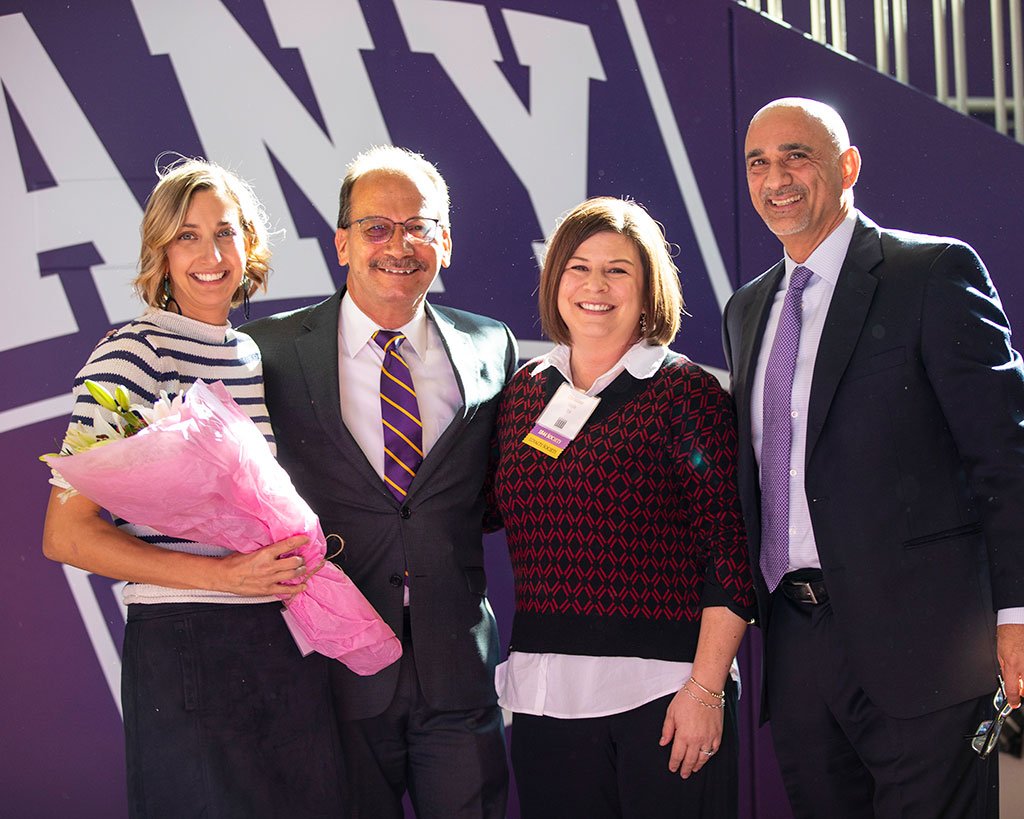 President Rodrigues, VP Fardin Sanai and Christy Doyle stand with Chrissie Binney holding a pink bouquet of flowers.