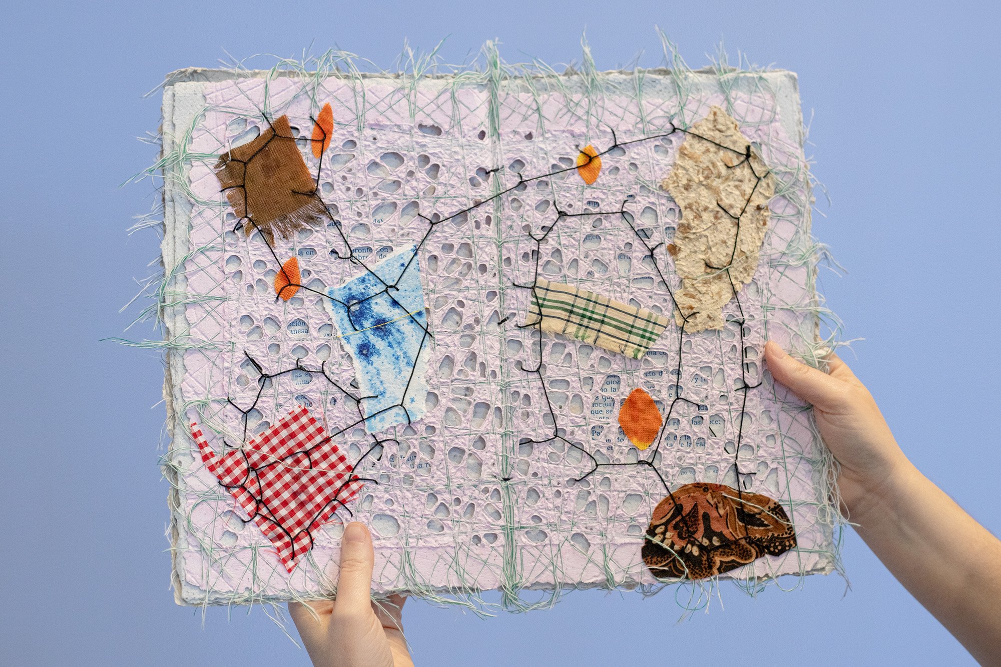 Hands holding up a publication made from handmade paper and stitching