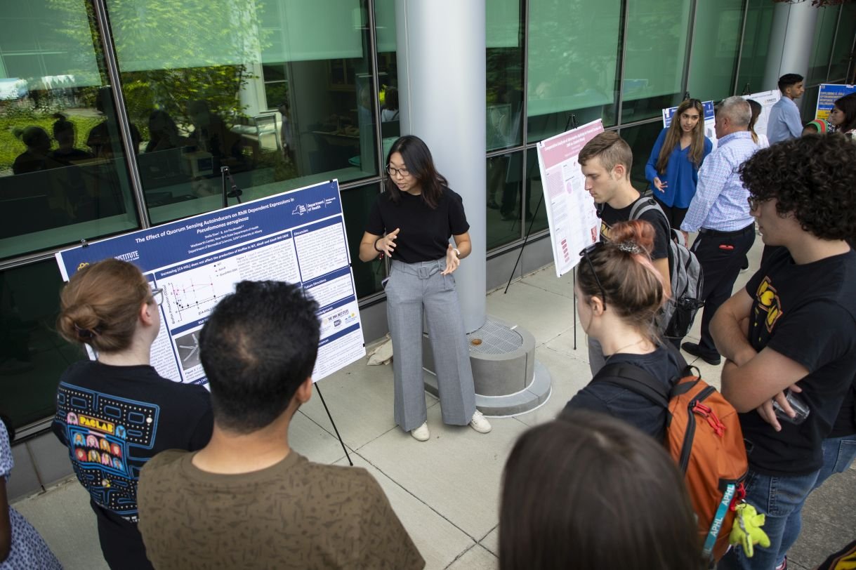 A student presents her research poster to a group of onlookers. 