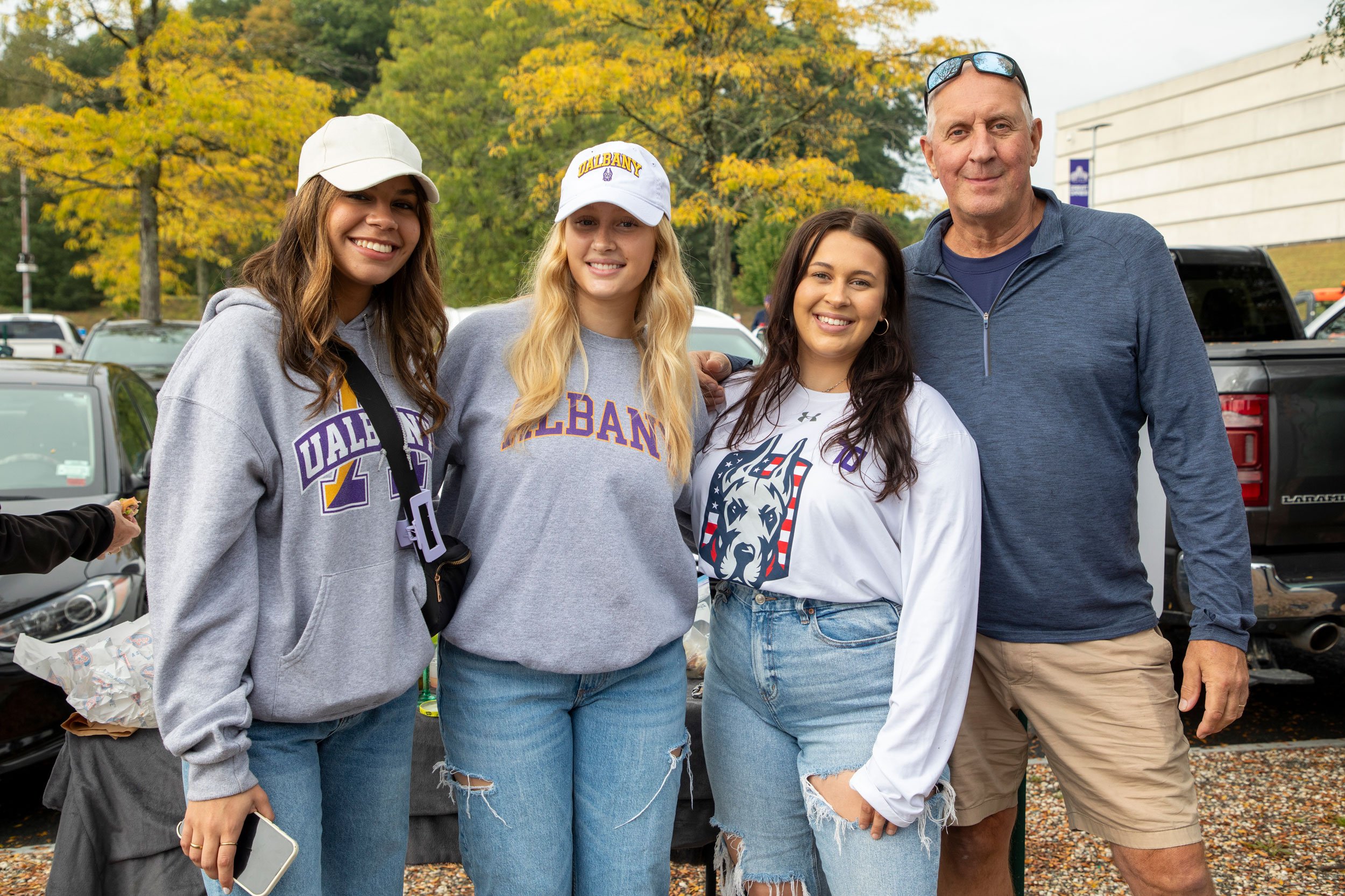 Four adults wearing UAlbany sweatshirts smile as they pose for a photo.