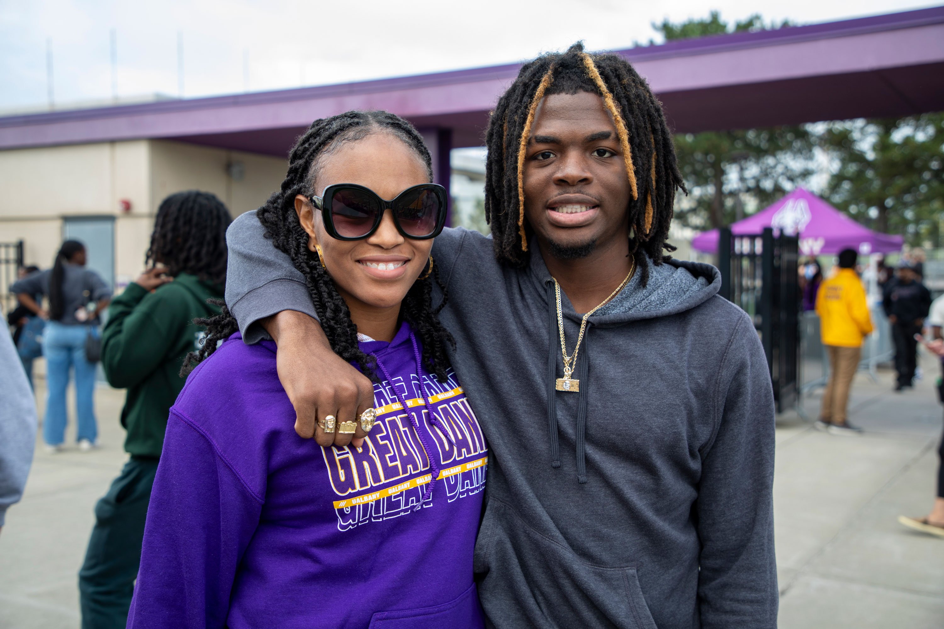 Two adults, one of whom is wearing a purple UAlbany sweatshirt, smile as they pose for a photo.