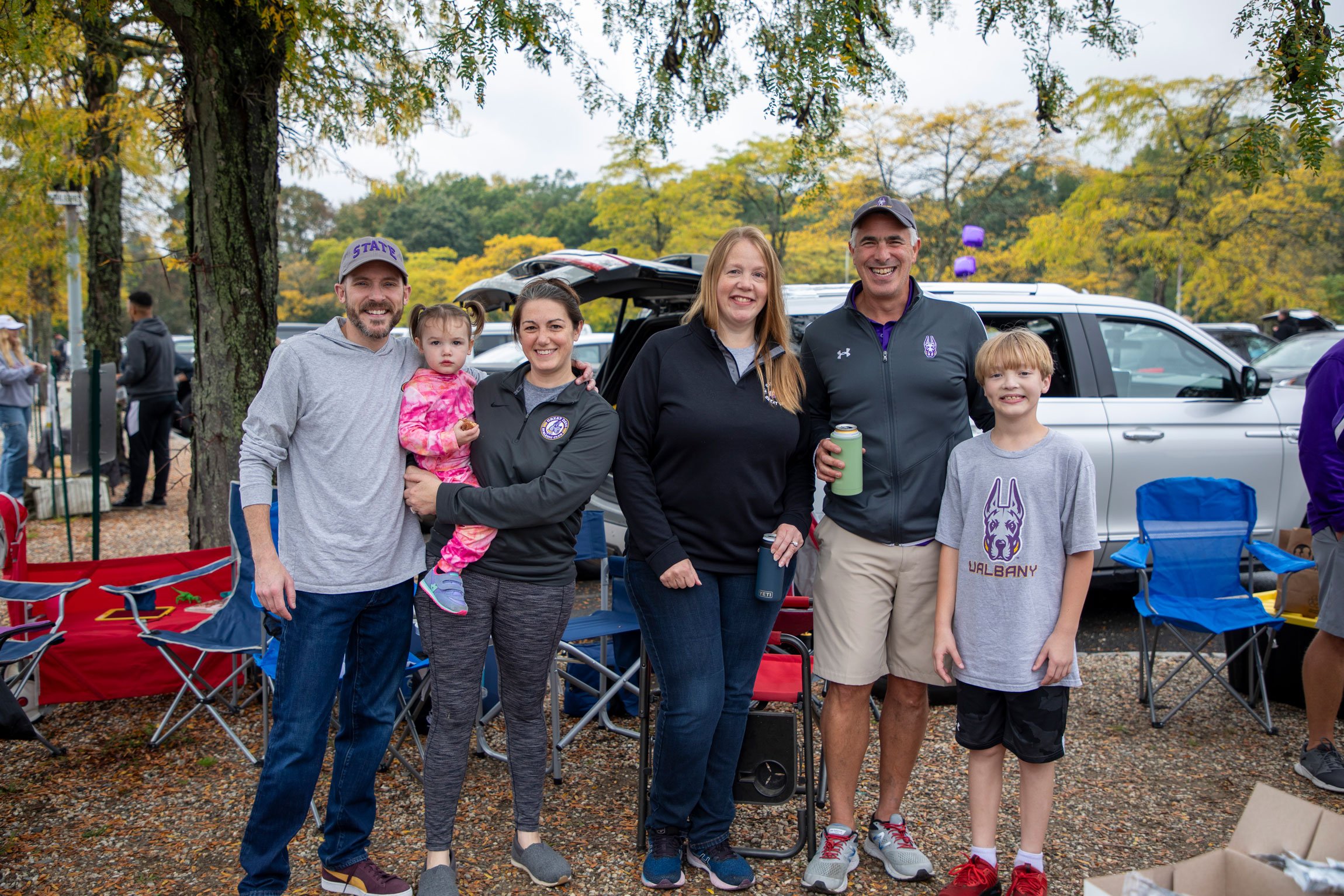 Four adults and two children smile as they pose for a photo while tailgating.