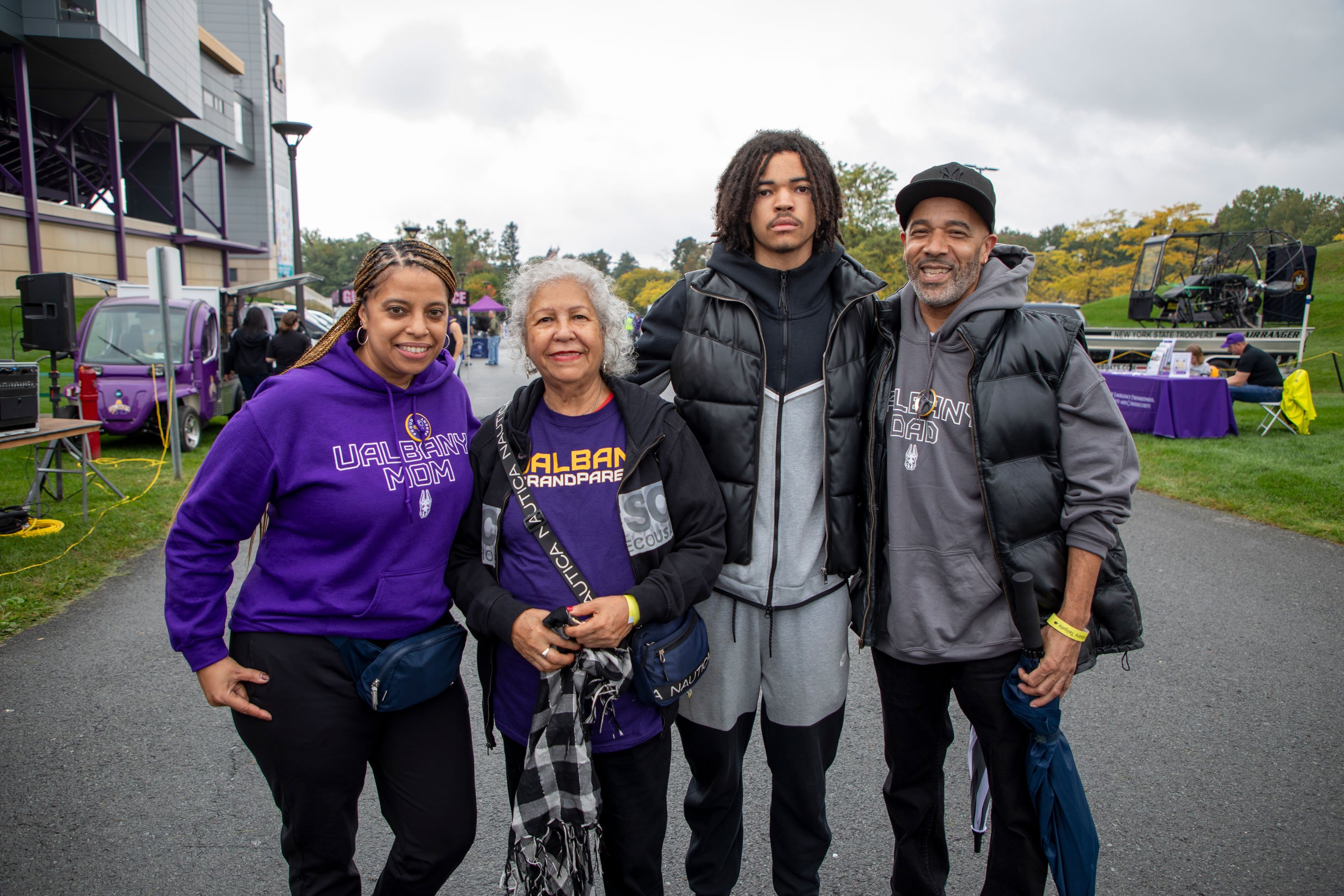 Four adults wearing UAlbany gear smile as they pose for a photo near the football stadium.