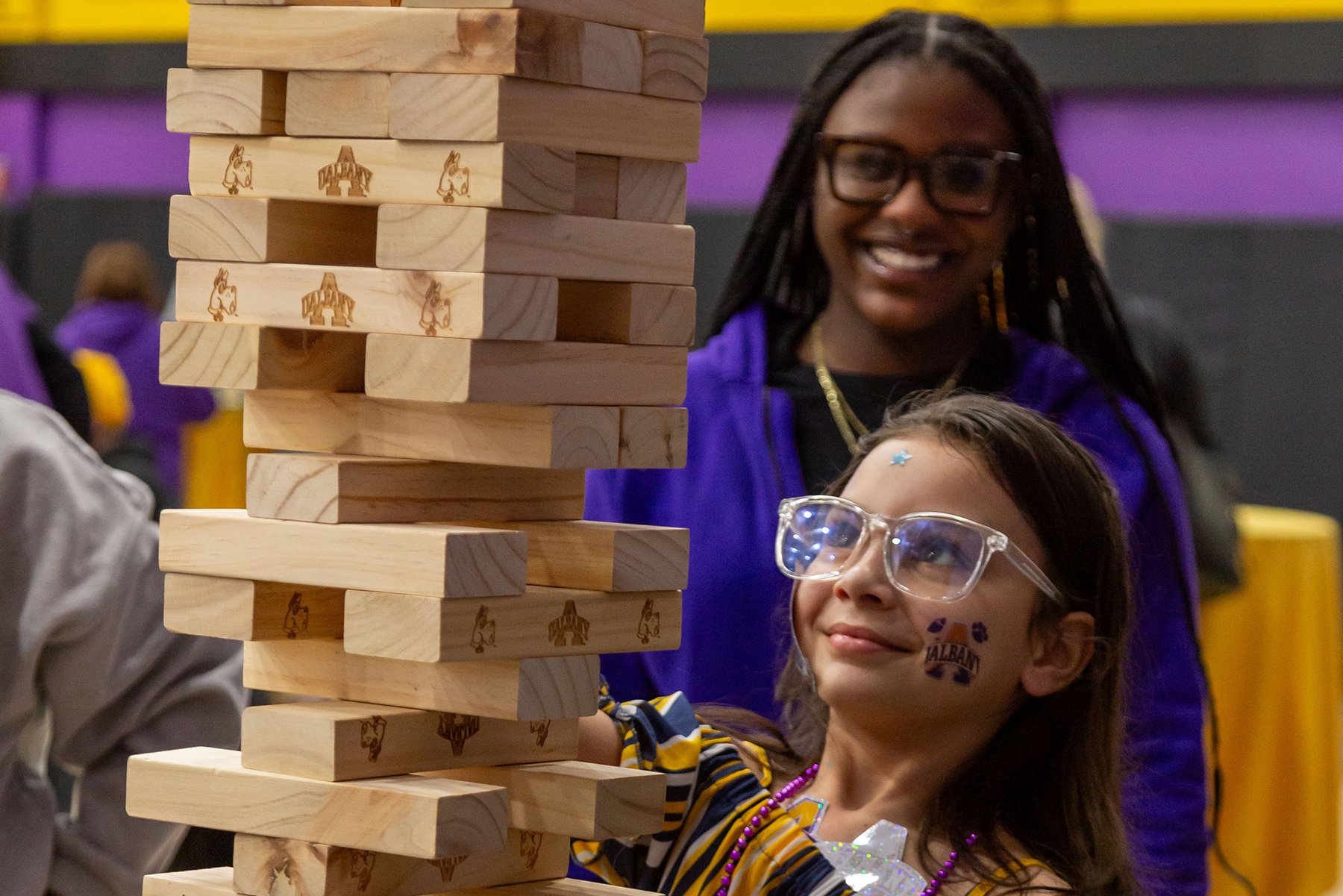 a young girl plays a large version of jenga with a UAlbany college student at the 2024 Big Purple Growl.
