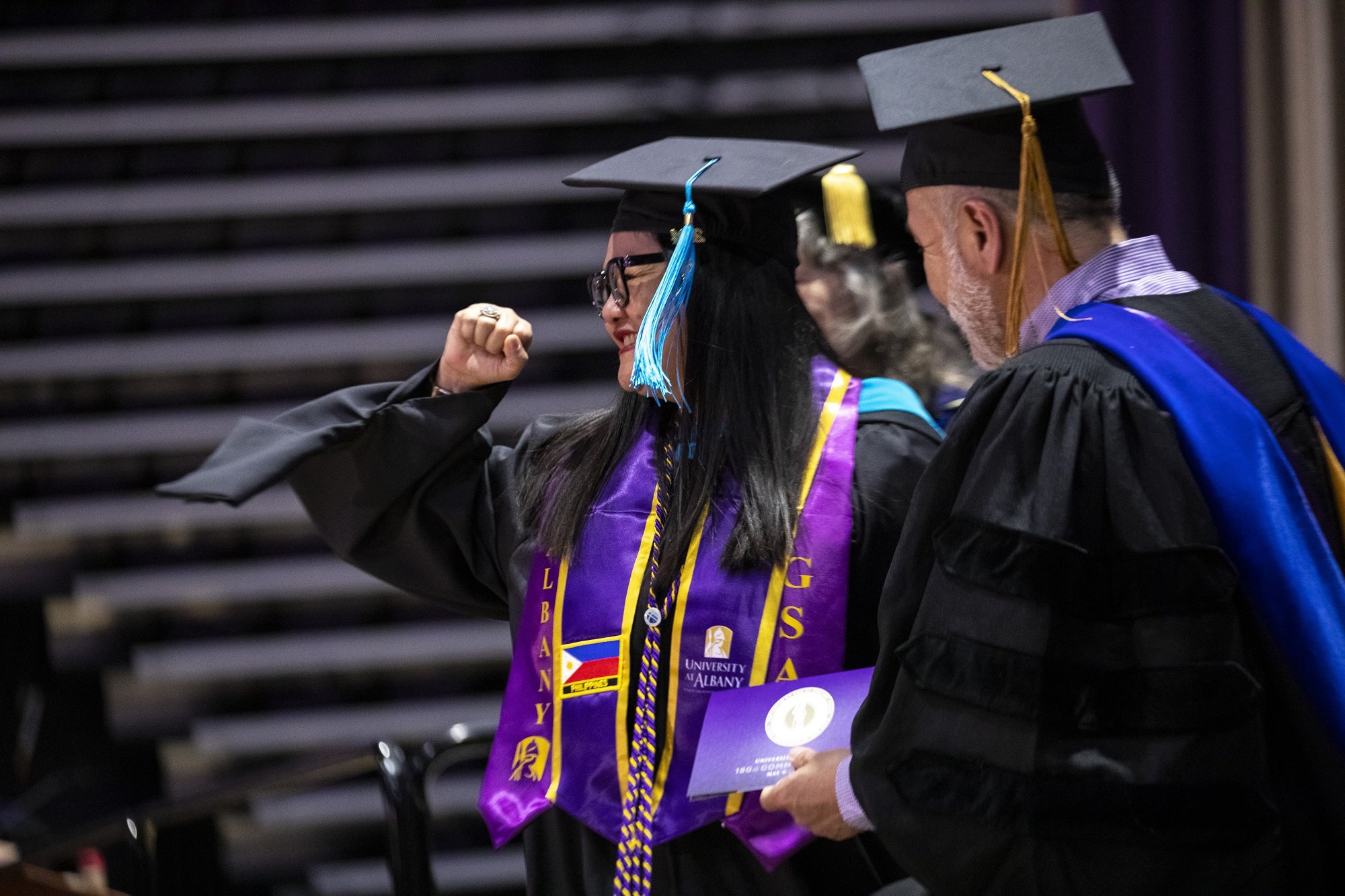 A UAlbany master's graduate pumps her fist as she walks across the stage.