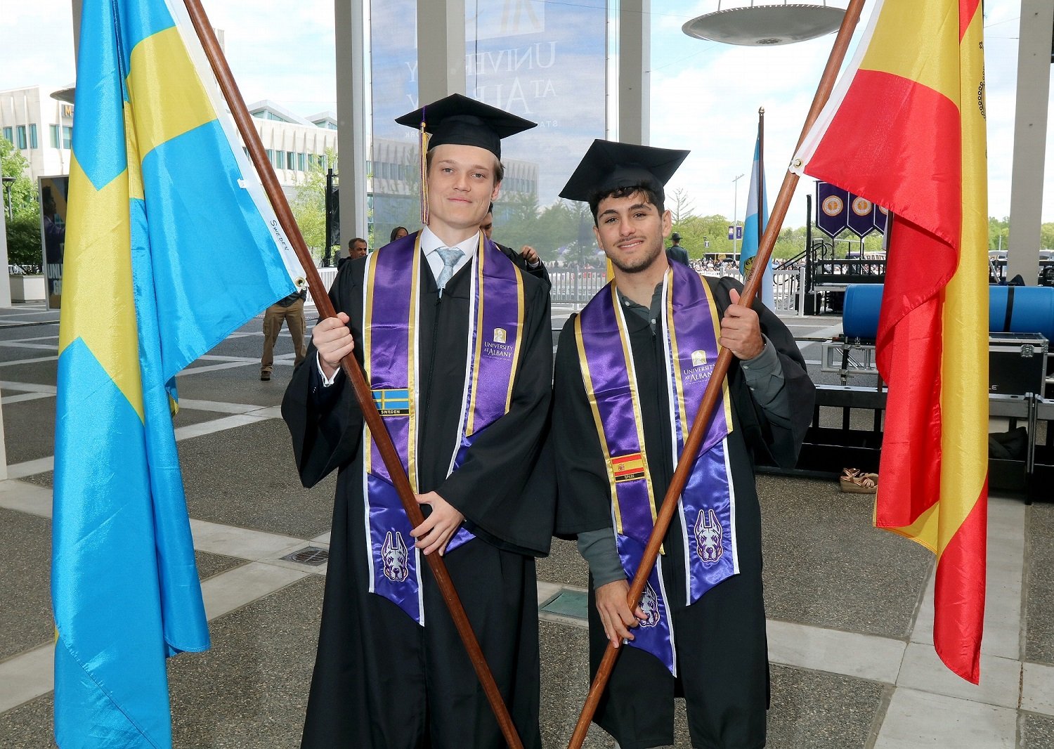 Two UAlbany international graduates hold up the flags of their home countries at the 2024 undergraduate commencement ceremony.