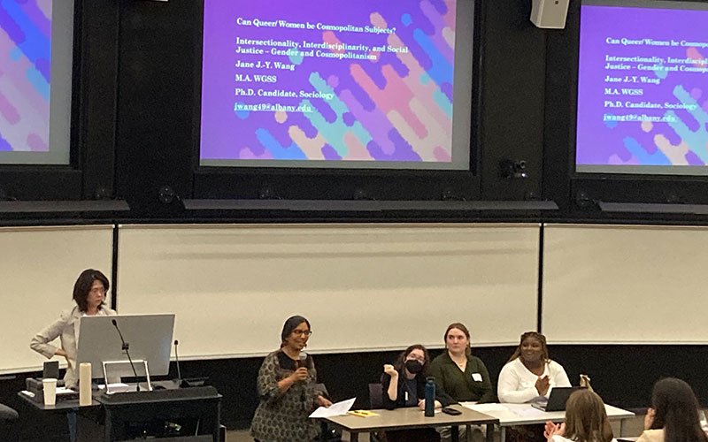 A student sits and holds a microphone while presenting on queer women as cosmopolitan subjects on a panel at UAlbany Showcase
