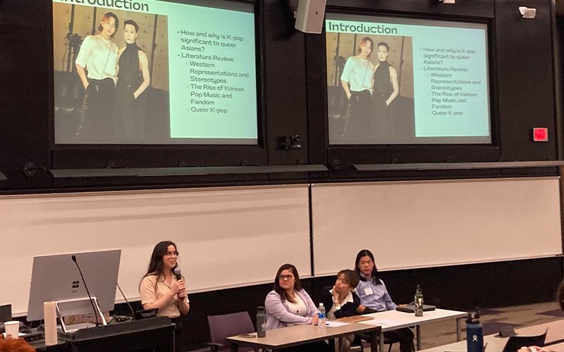 A student stands and holds a microphone while presenting on k-pop on a panel at UAlbany Showcase