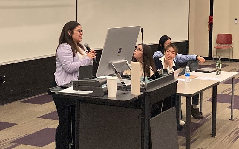 A student stands and holds a microphone while presenting on a panel at UAlbany Showcase