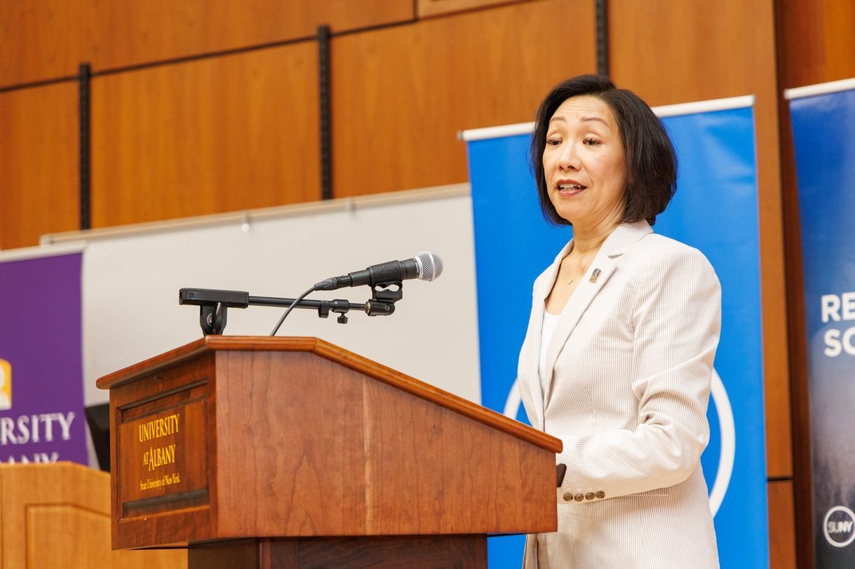 A woman wearing a cream suit makes remarks from a wooden podium.