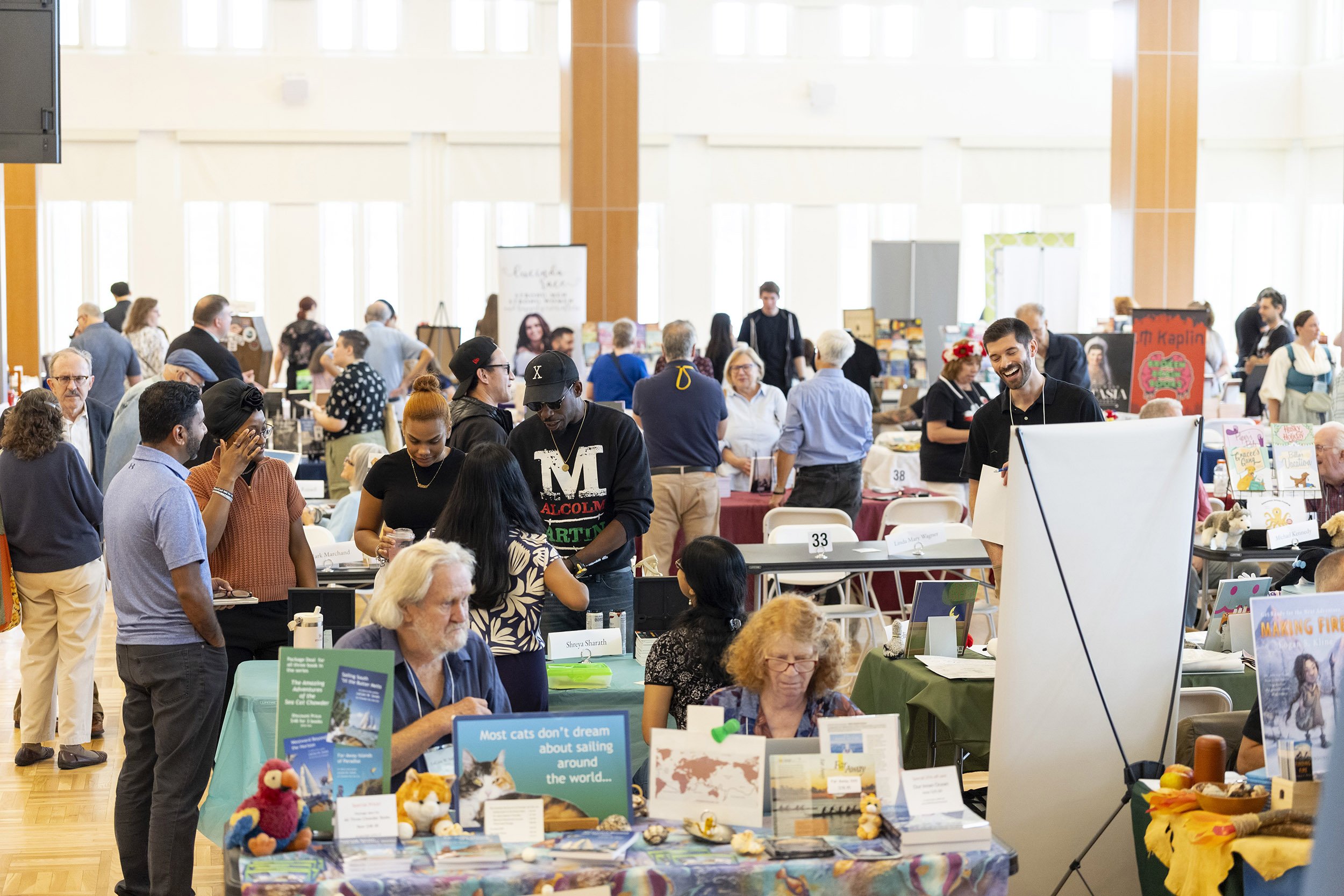 A large group of people mingle amid rows of books on tables indoors.