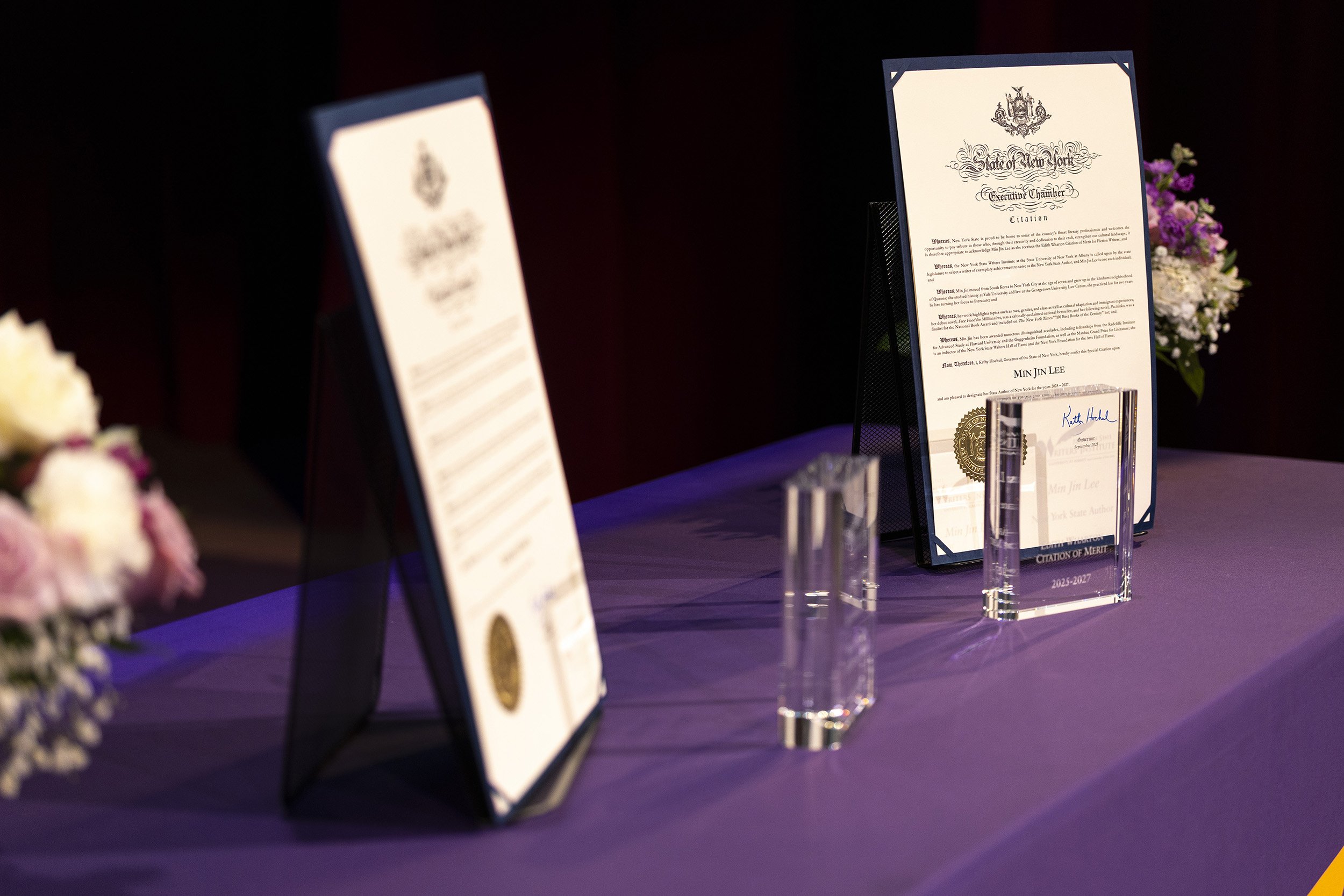 A table with a purple table cloth holds two proclamations and two glass awards indoors.