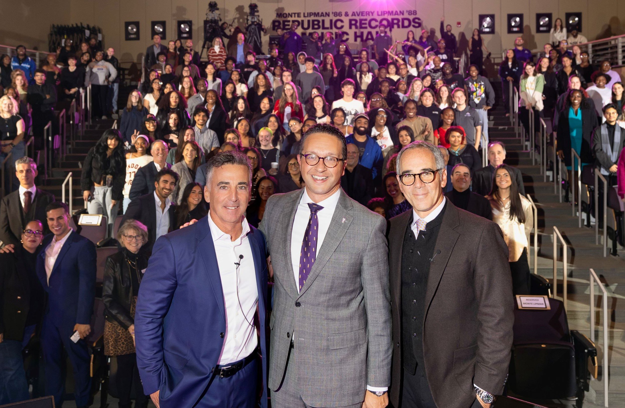 Avery Lipman, Mike Christakis and Monte Lipman stand in front of a packed auditorium of students for a photo celebrating the opening of a music hall in their honor.