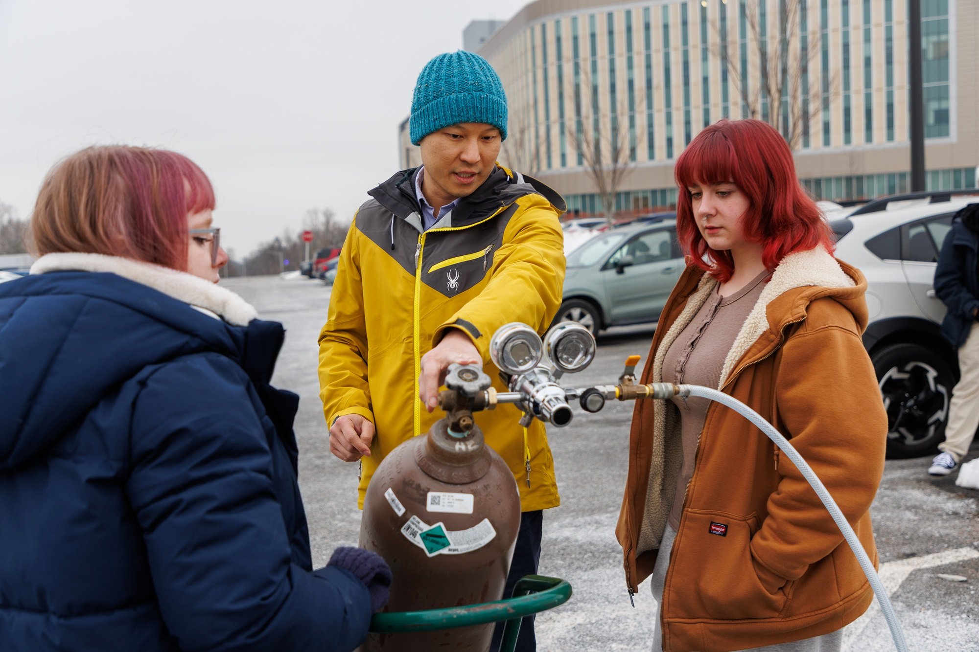 Professor Brian Tang supports students will filling up a weather balloon with helium.