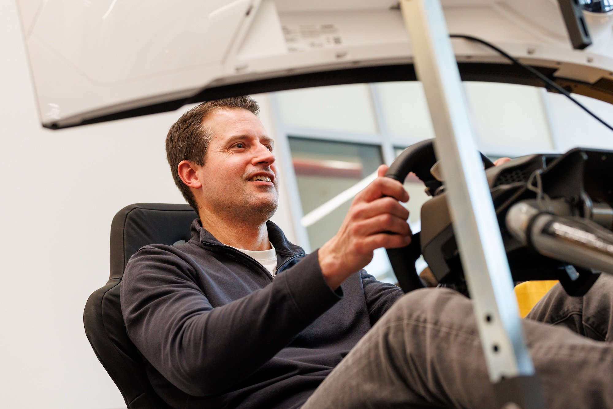 A man smiles as he grips a steering wheel 