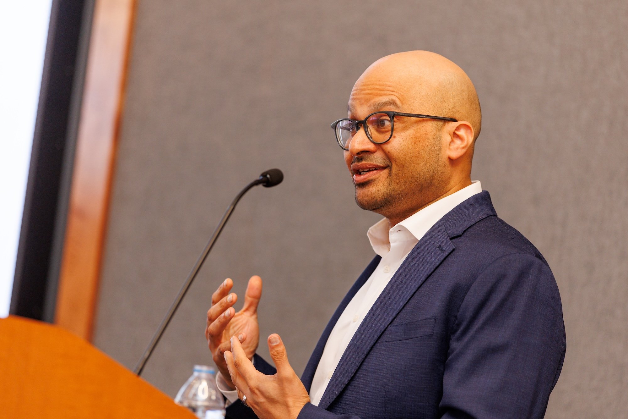A man wearing glasses gestures as he speaks into a microphone