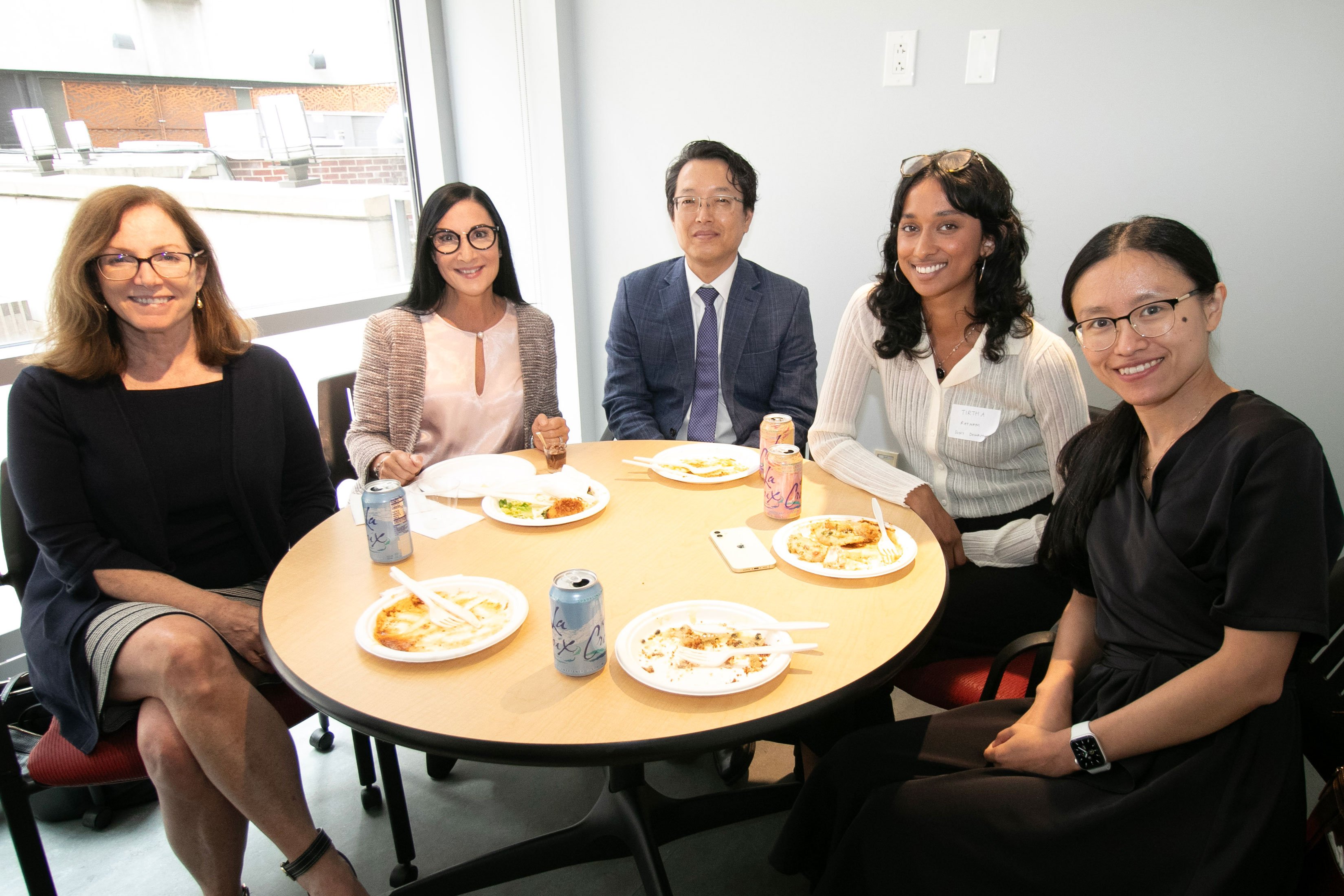 Five individuals sitting at a table with food smiling at the 2nd Annual Summit for the Global Center in AI Mental Health at the Suny Global Center in NYC.