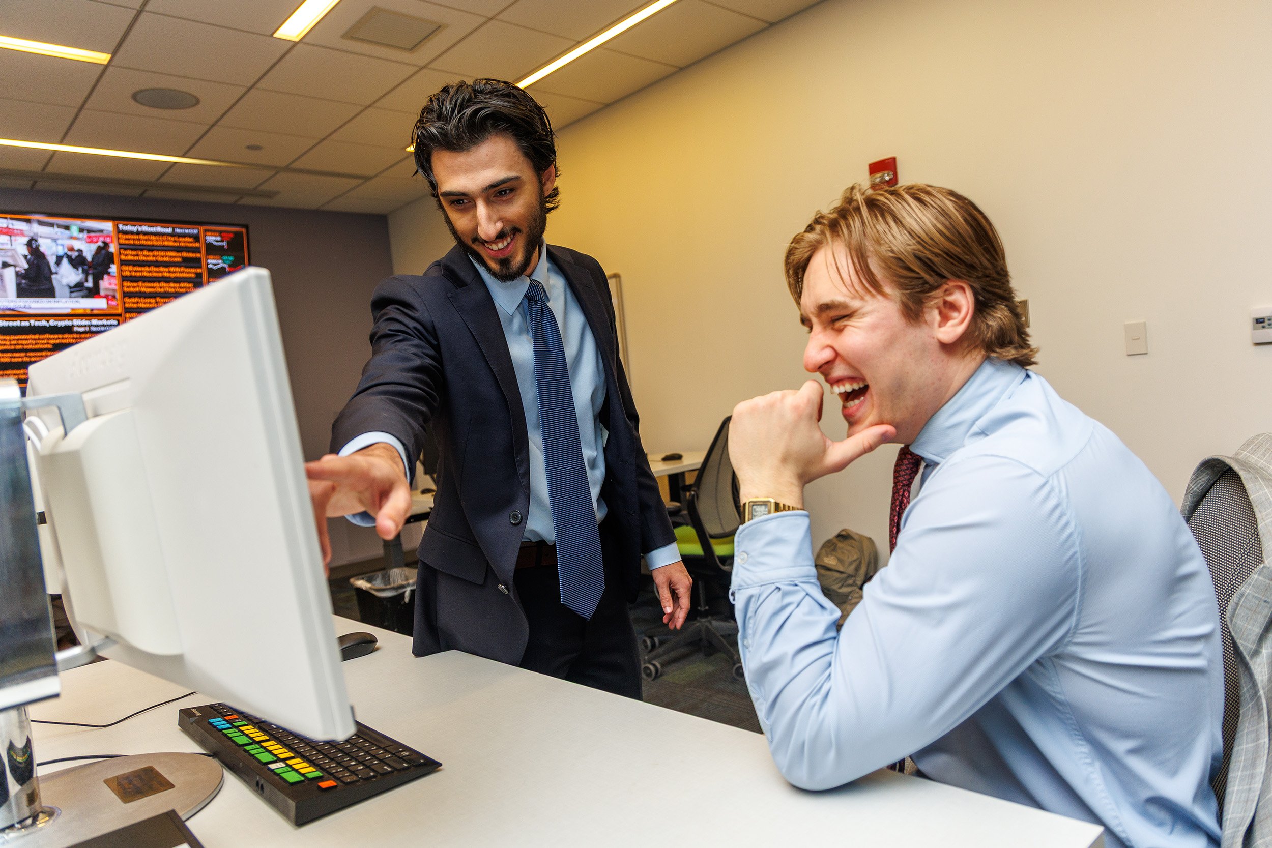 Two young men sit at a terminal inside of the investment suite at the Massry School of Business