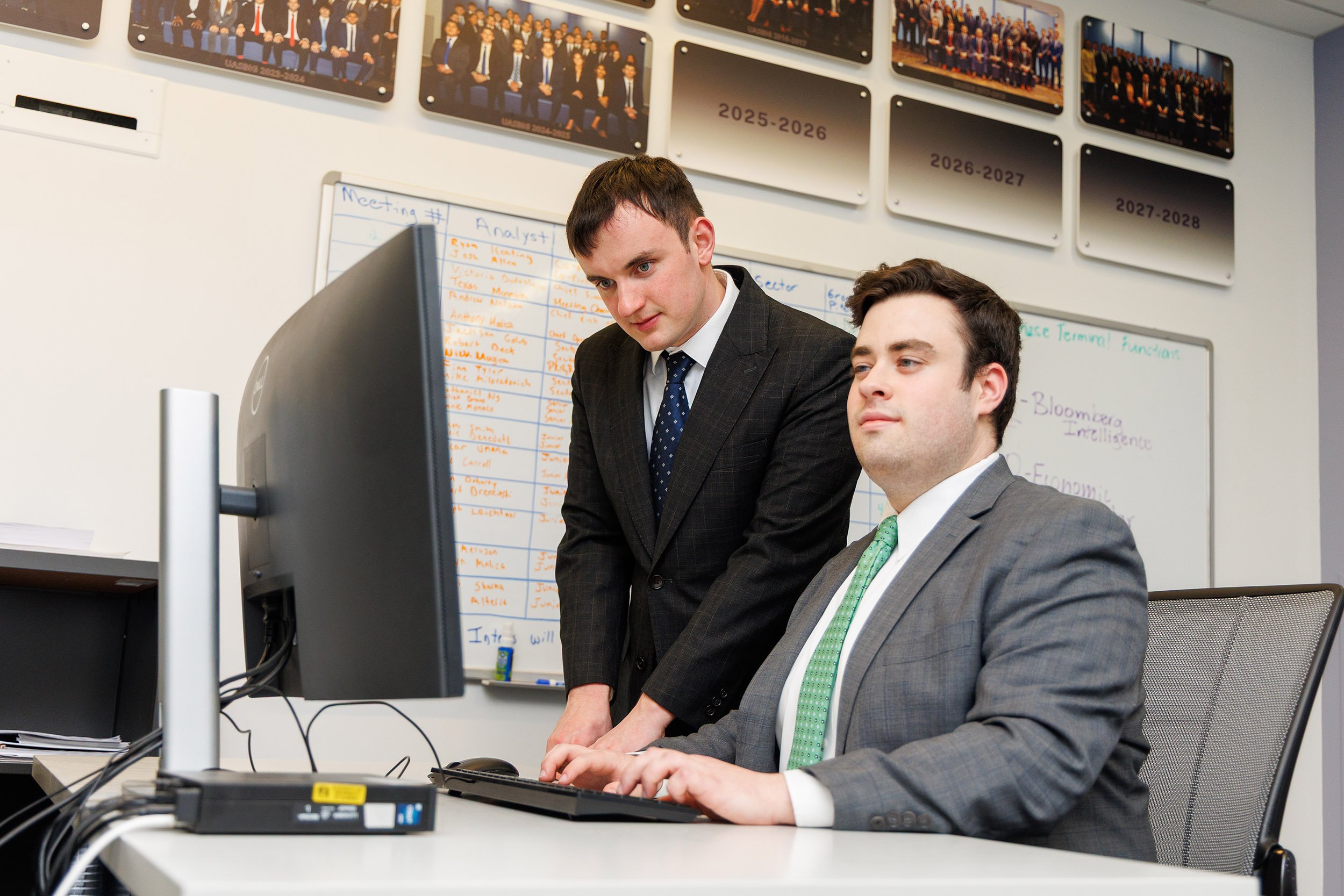 Two young men sit at a Bloomberg terminal inside of the investment suite at UAlbany's Massry School of Business