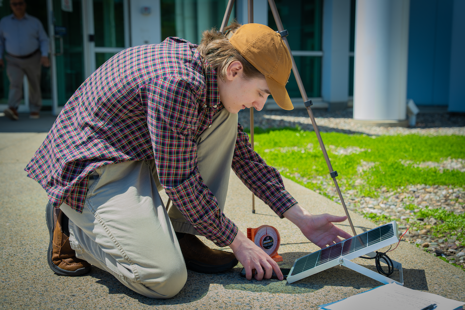 A young man gathers around a solar panel for a workshop on energy storage technologies