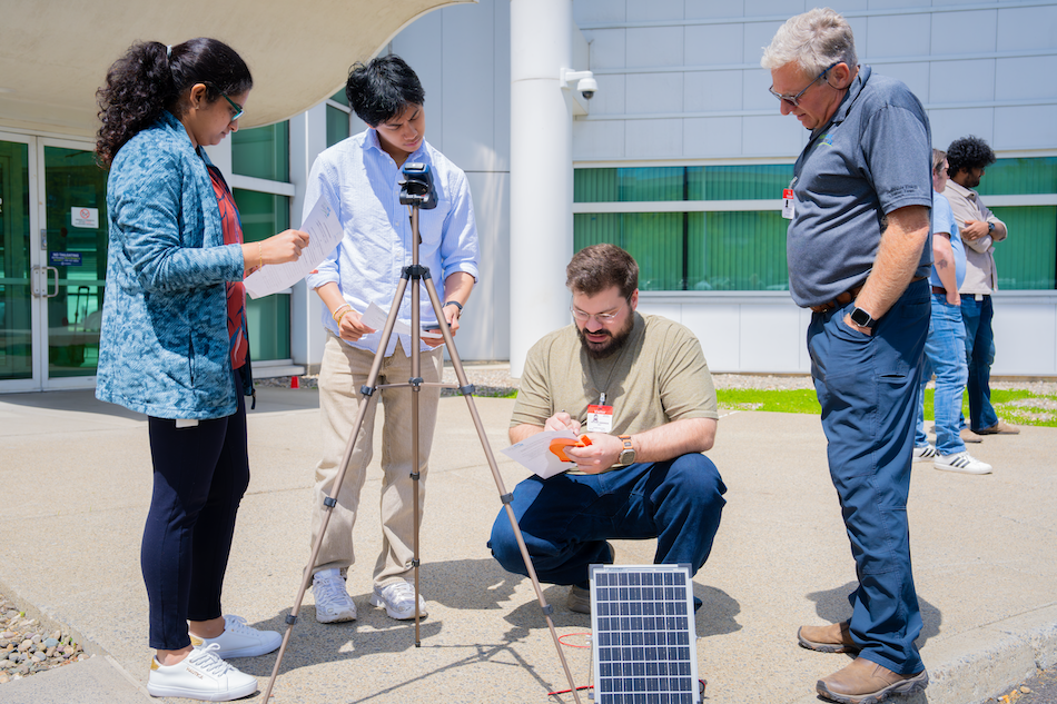 People gather around a solar panel for a workshop on energy storage technologies